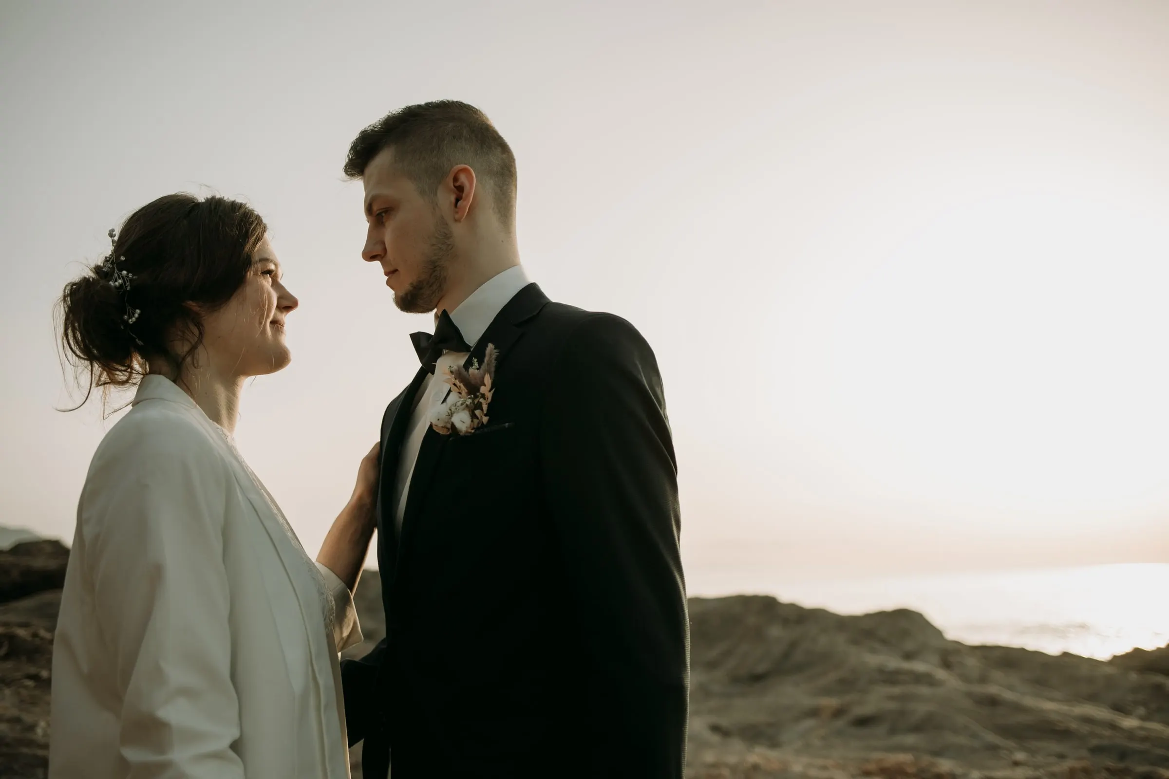 La novia apoya la mano en el pecho del novio mientras se miran junto al mar