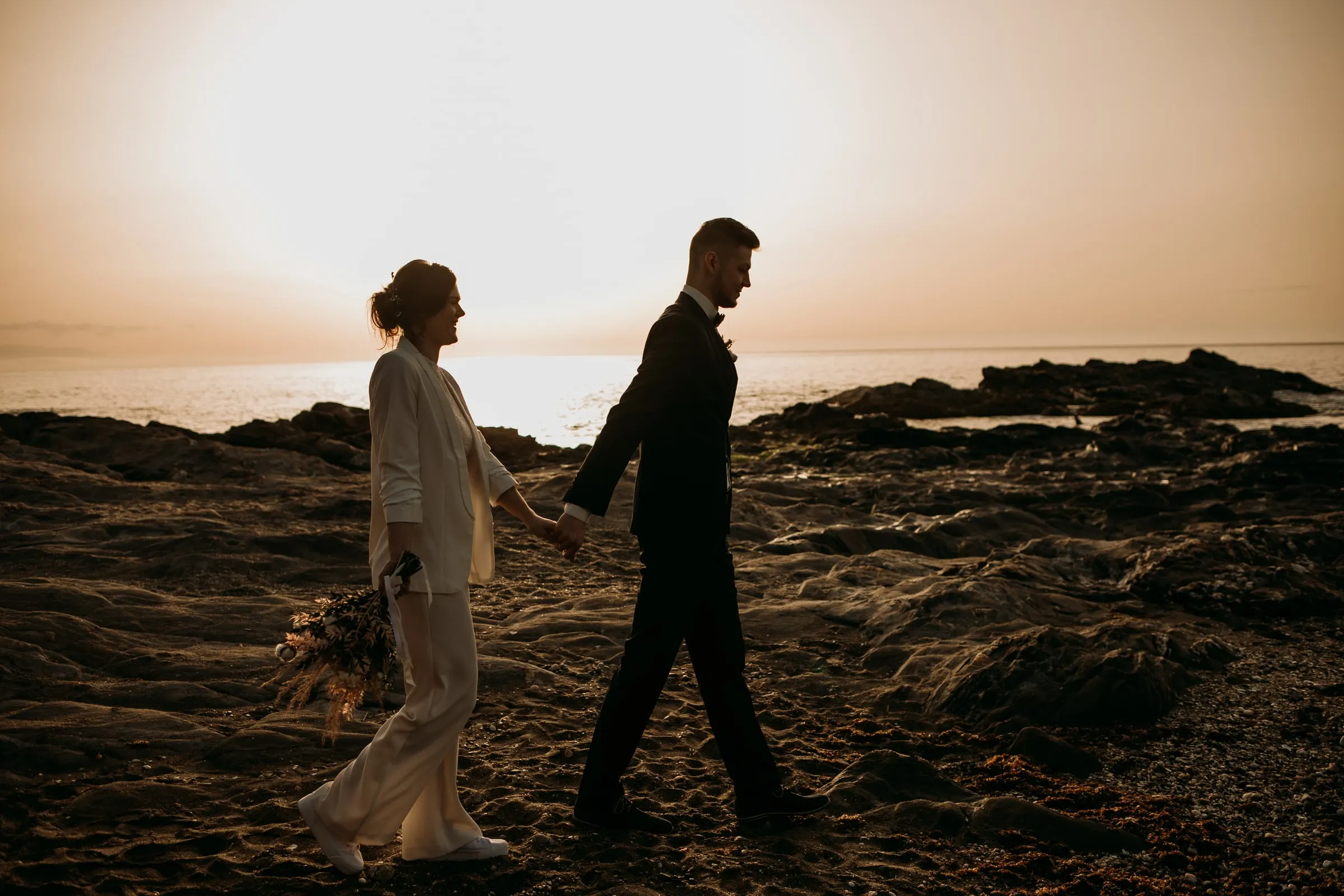 Siluetas de los novios caminando de la mano por las rocas hacia el sol