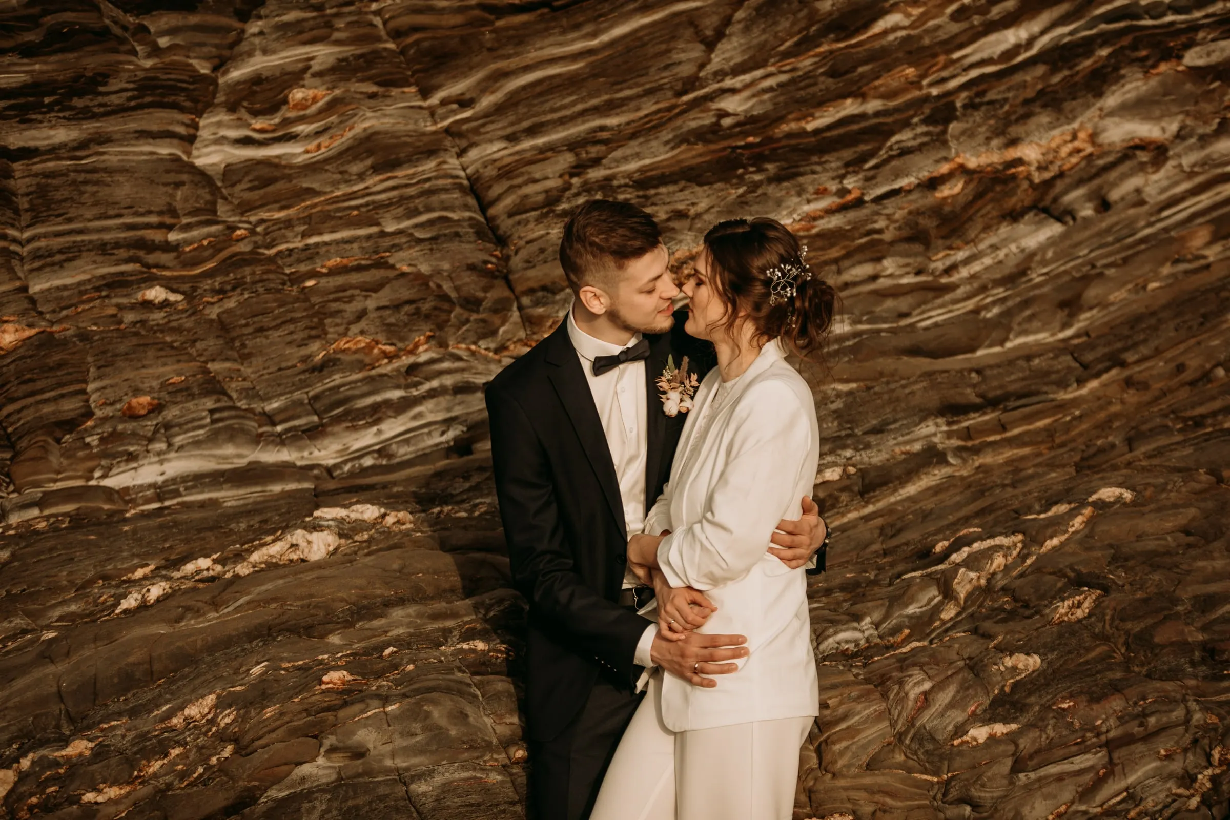 Beso de los novios ante una pared de roca a capas y vetas en la playa, Costa del Sol