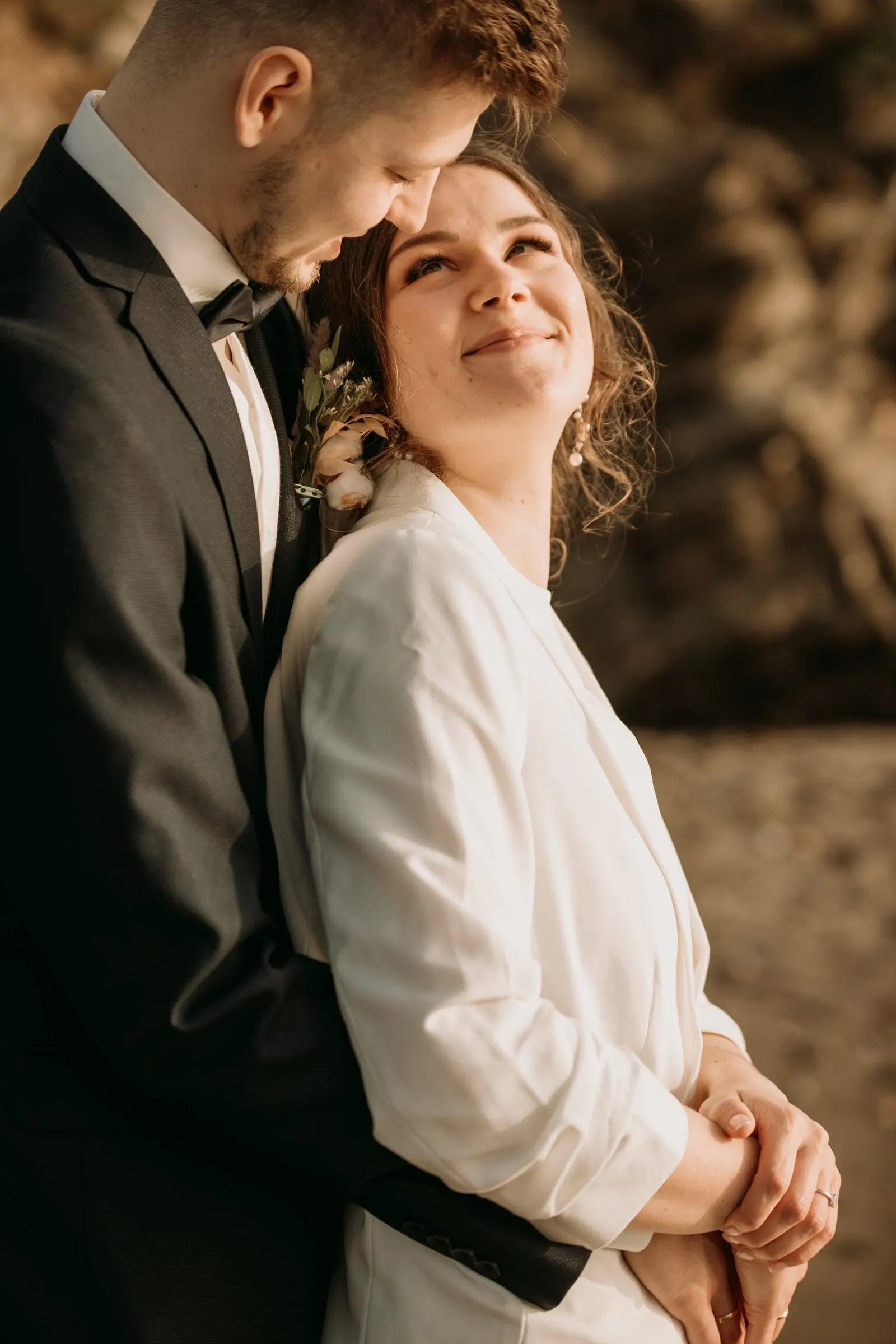 La novia mira hacia arriba y sonríe mientras el novio la abraza por detrás