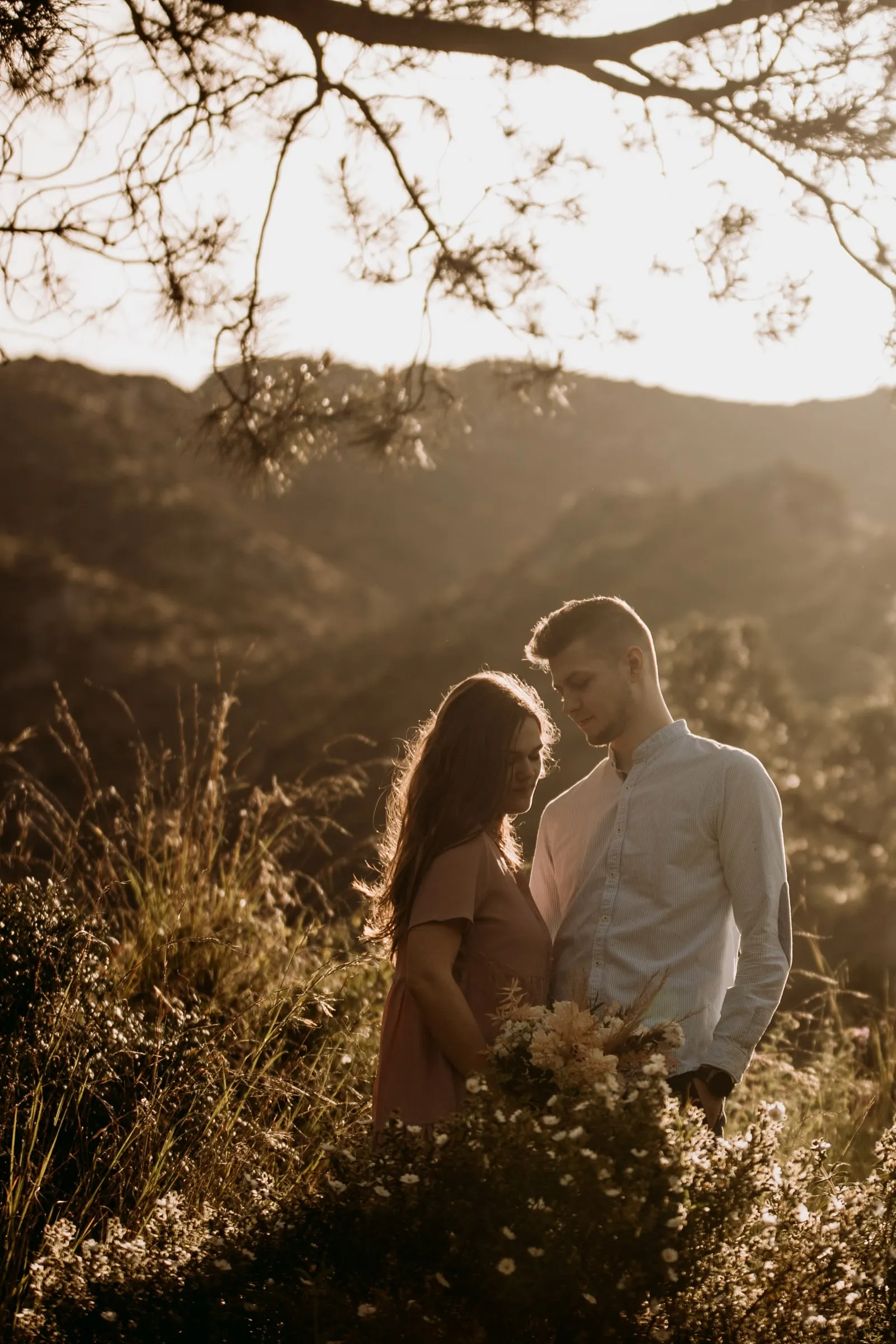La pareja frente a frente bajo un pino con la sierra a lo lejos