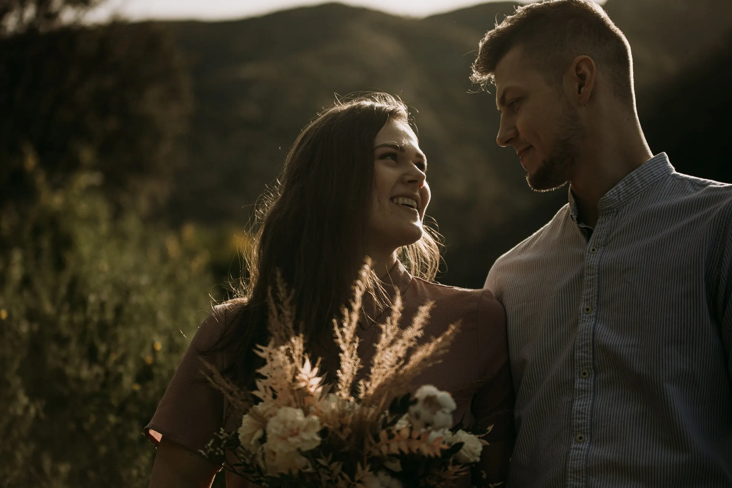 La pareja ríe junta con un ramo de hierbas secas y la sierra detrás
