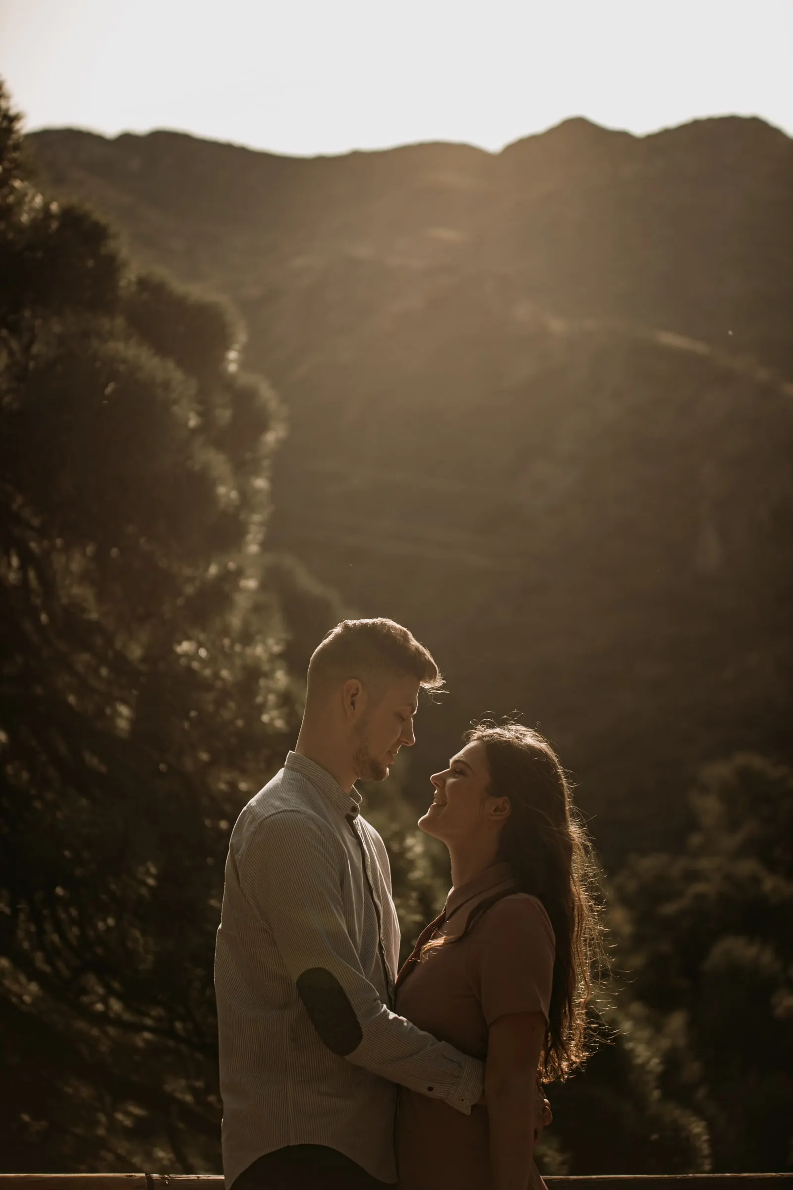 La pareja a punto de besarse a contraluz, con un valle arbolado y empinado detrás, Costa del Sol