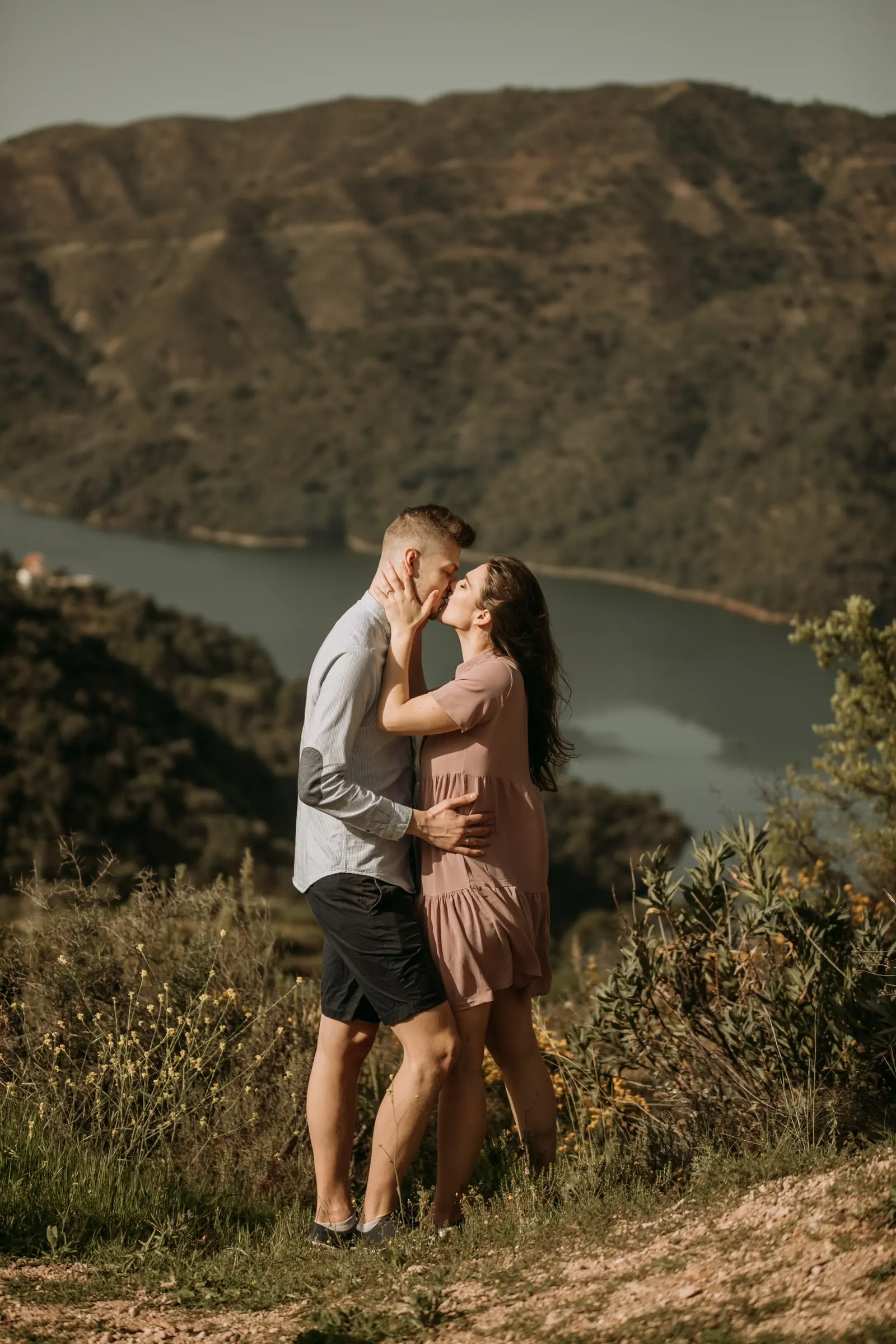 Beso de la pareja en lo alto de una loma sobre un embalse entre montes verdes, preboda en la Costa del Sol