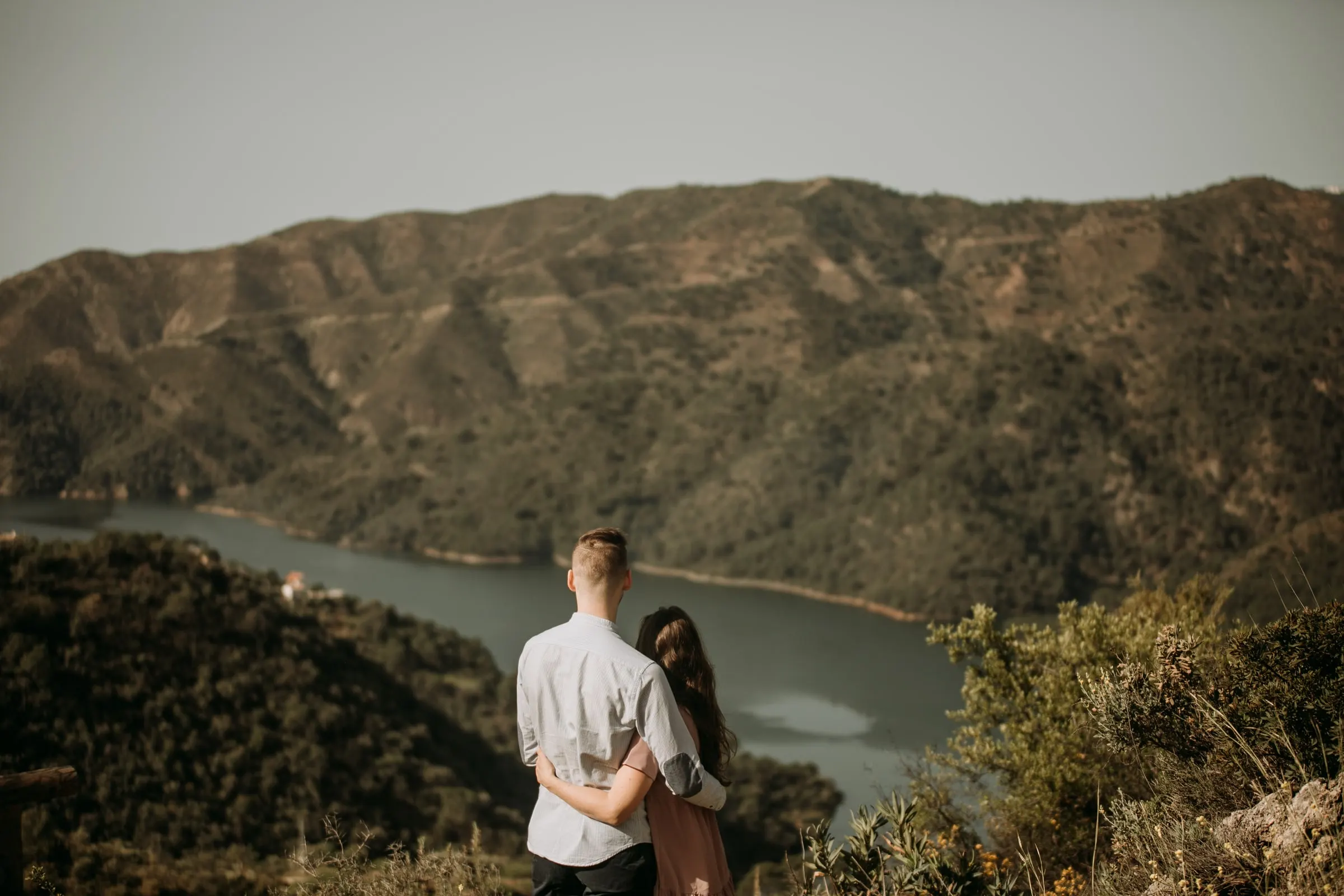 Couple from behind looking out over a reservoir winding between wooded hills