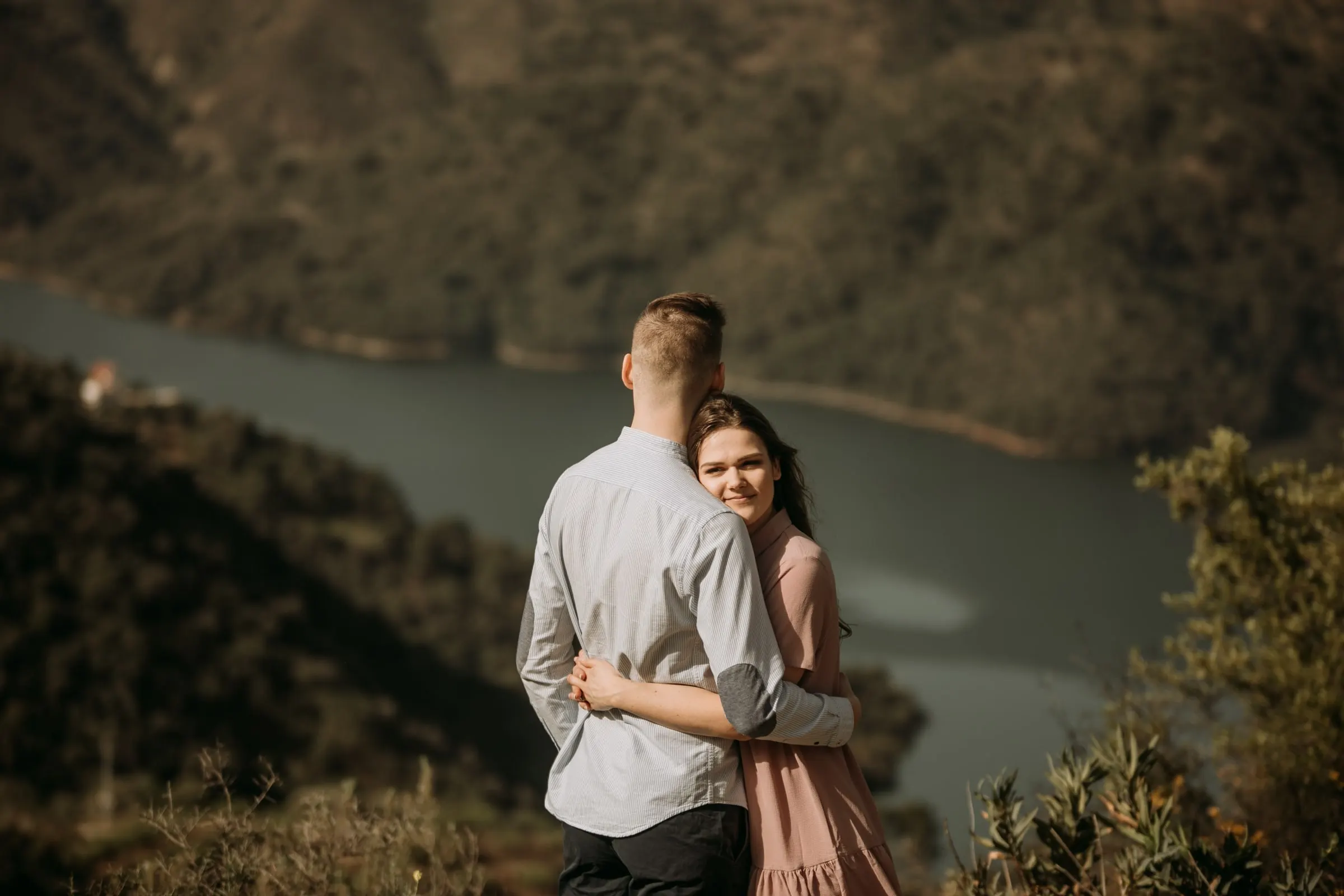 La futura novia sonríe por encima del hombro de su prometido, con el embalse desenfocado abajo
