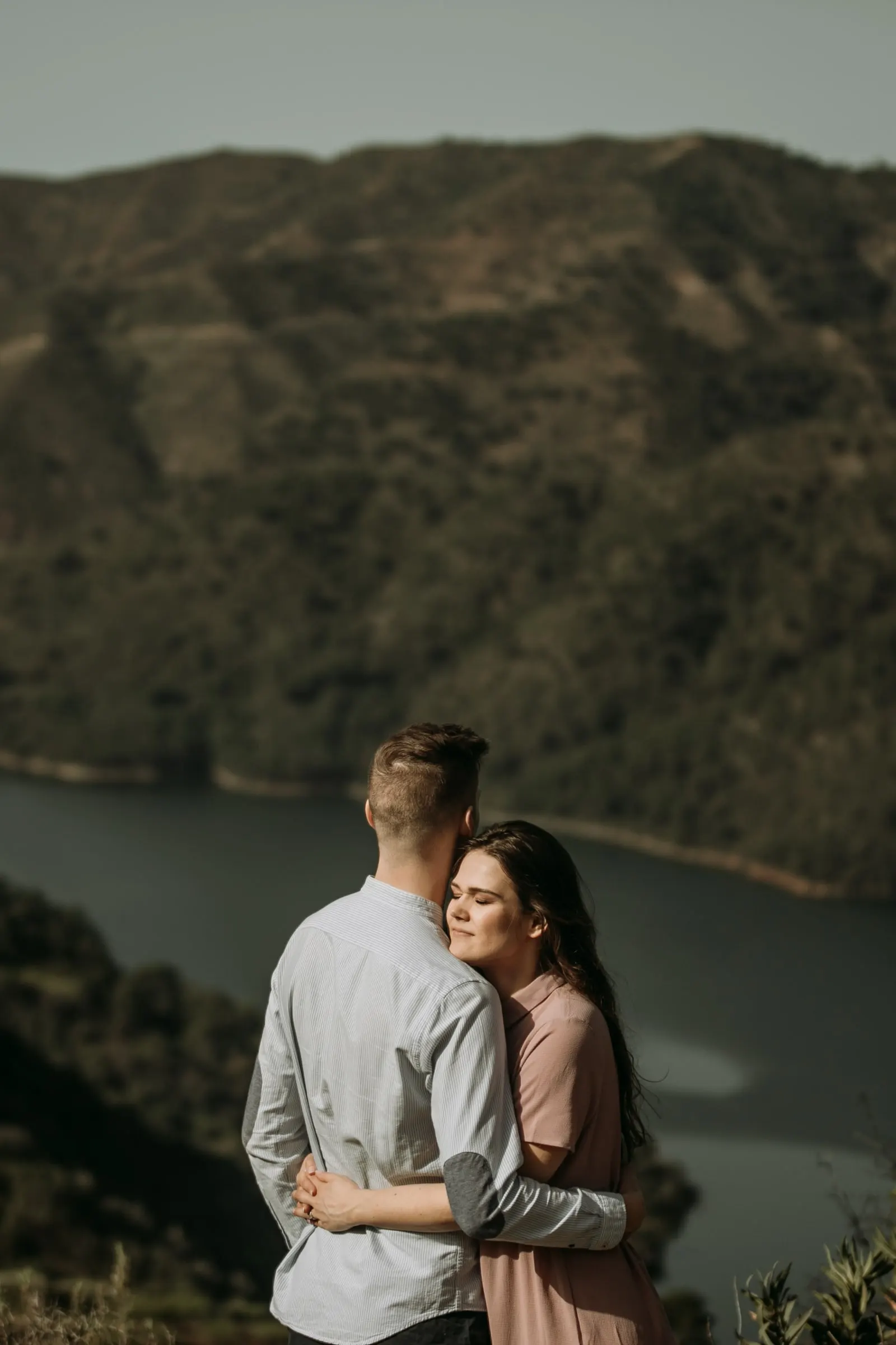 La pareja abrazada en un mirador sobre el agua, con la cabeza de ella apoyada en él