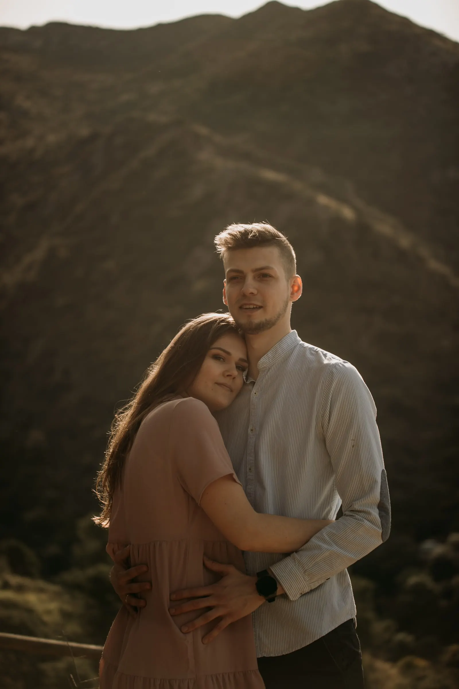 La pareja abrazada sonríe a cámara con un monte detrás