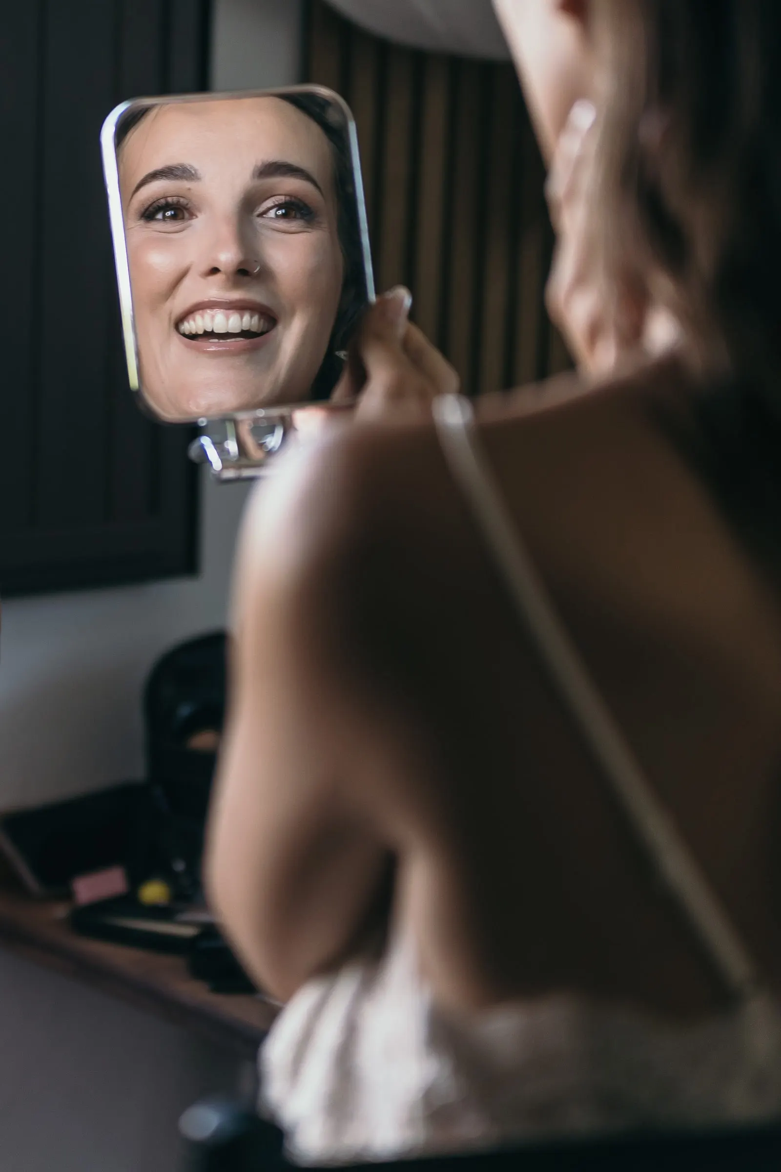 Bride smiling into a hand mirror after her make-up