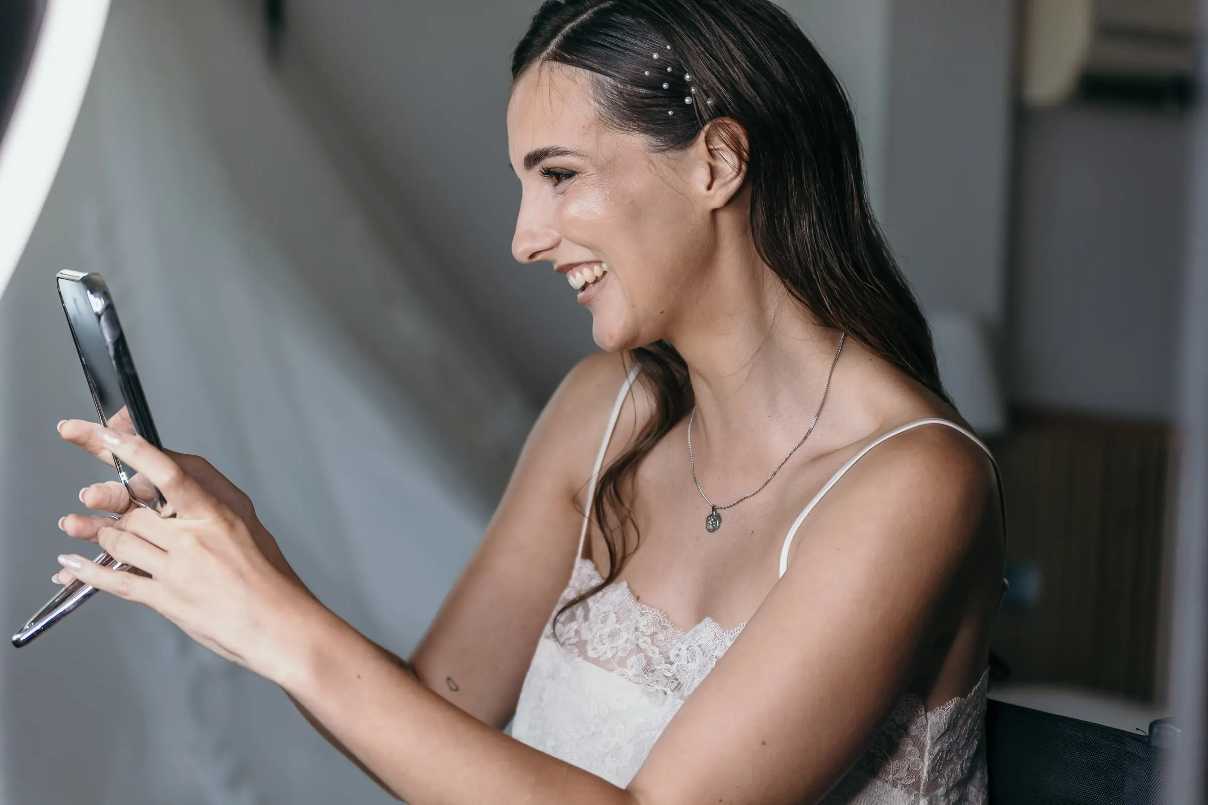 Bride laughing at her reflection in a phone screen beside the ring light