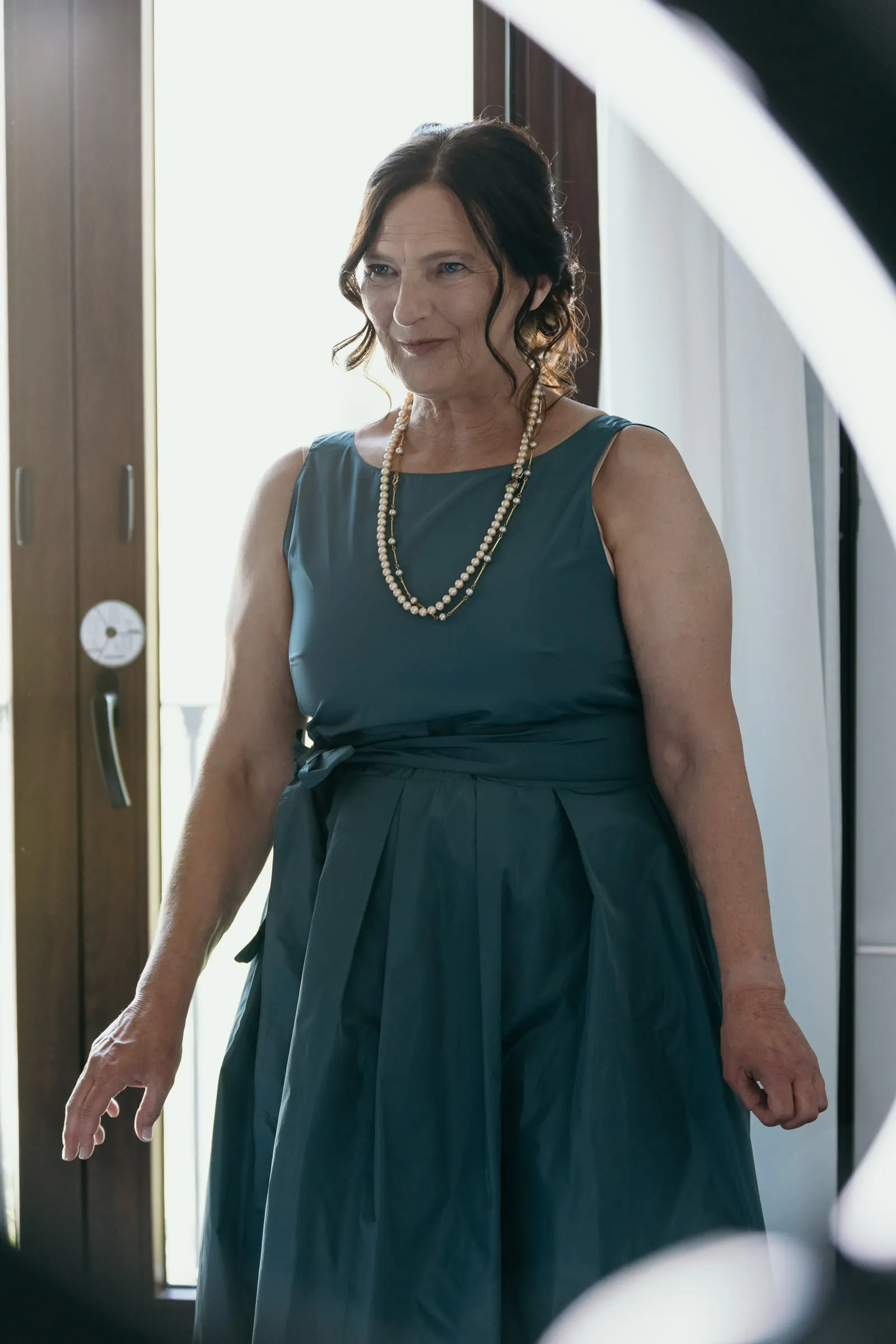 Woman in a teal dress and a long pearl necklace walking into the bridal room