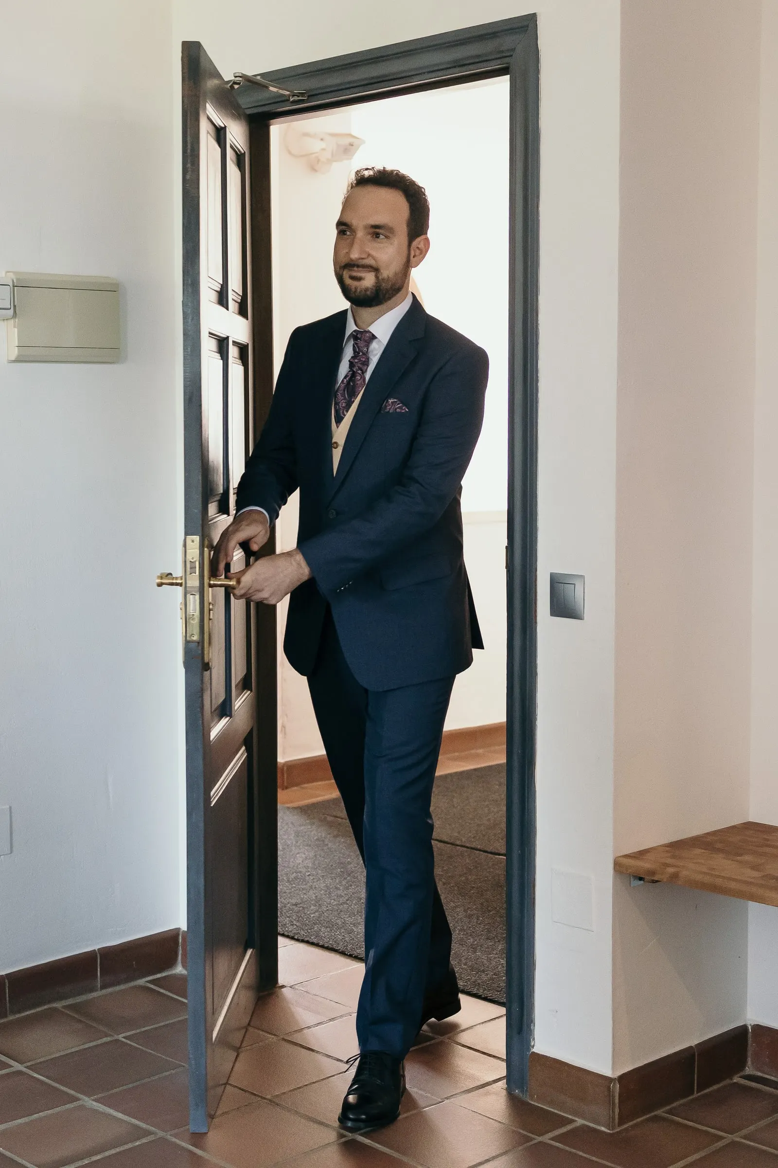 Groom smiling as he opens a blue wooden door on his way to see the bride