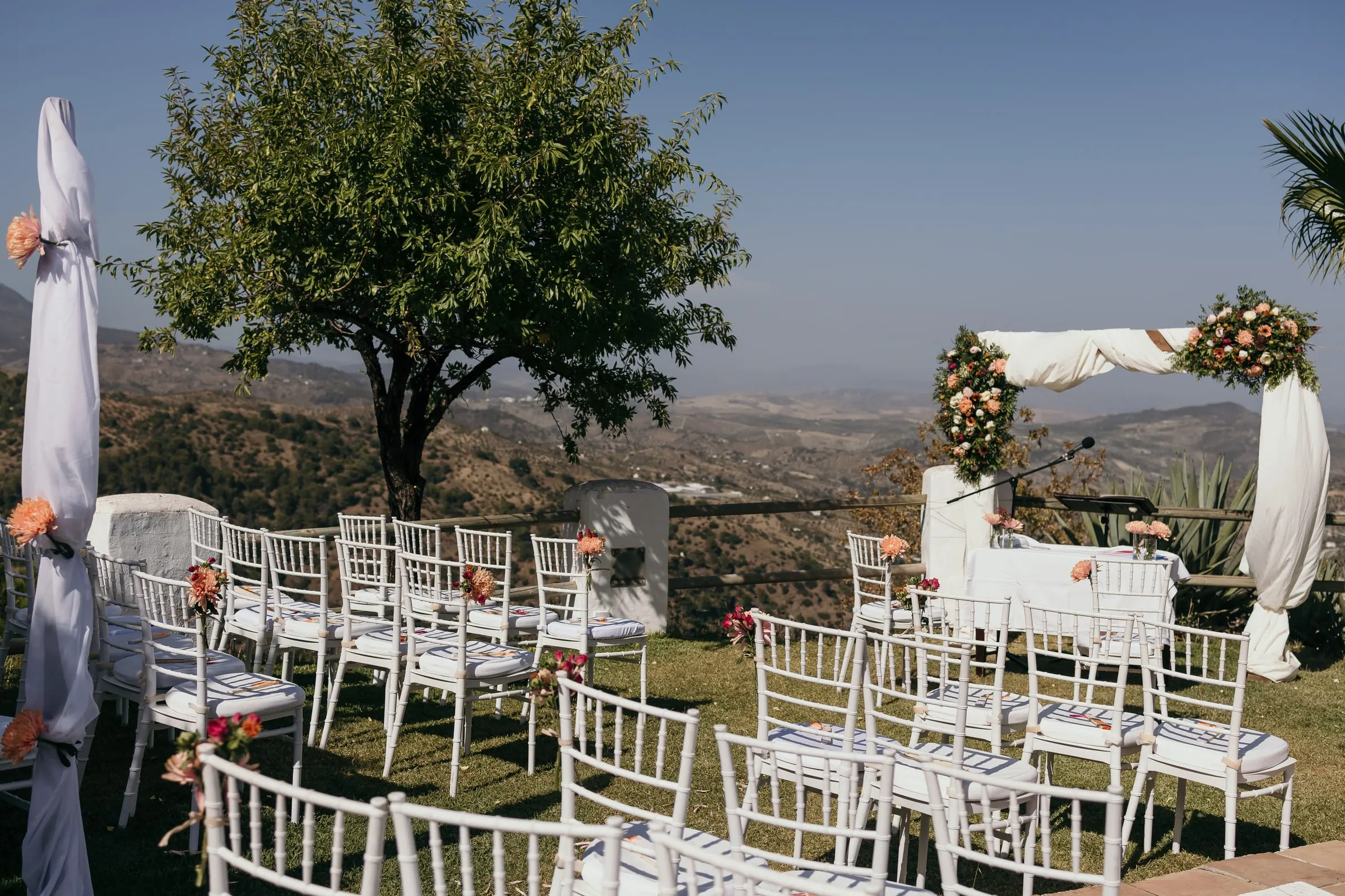 White chairs and a floral arch on the lawn overlooking the hills, at a hillside finca on the Costa del Sol