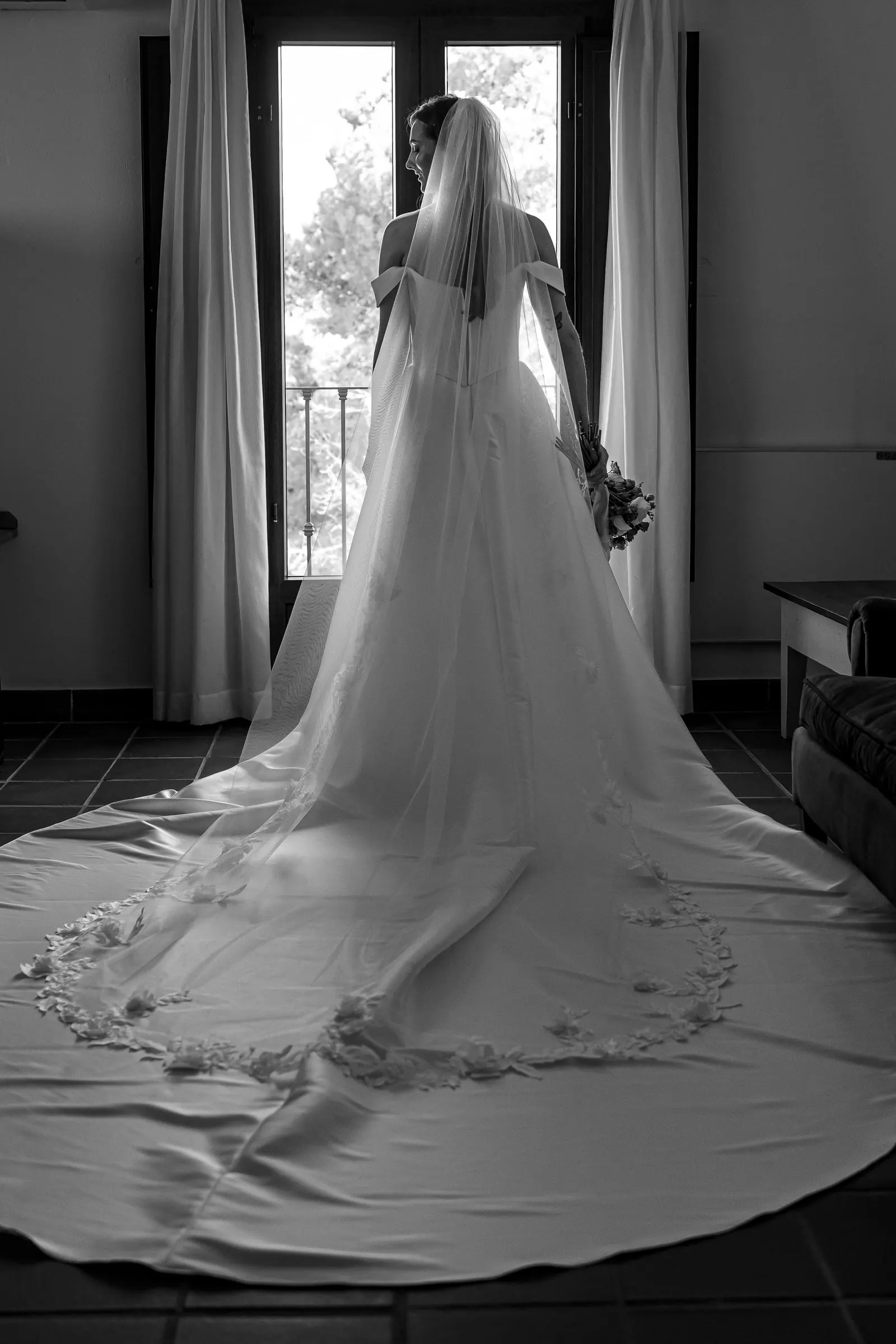 Black and white of the bride's train and lace-edged veil spread across the floor by the window