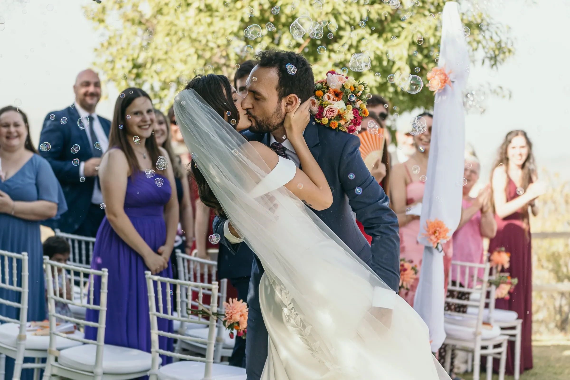 Groom kissing the bride in the aisle among soap bubbles