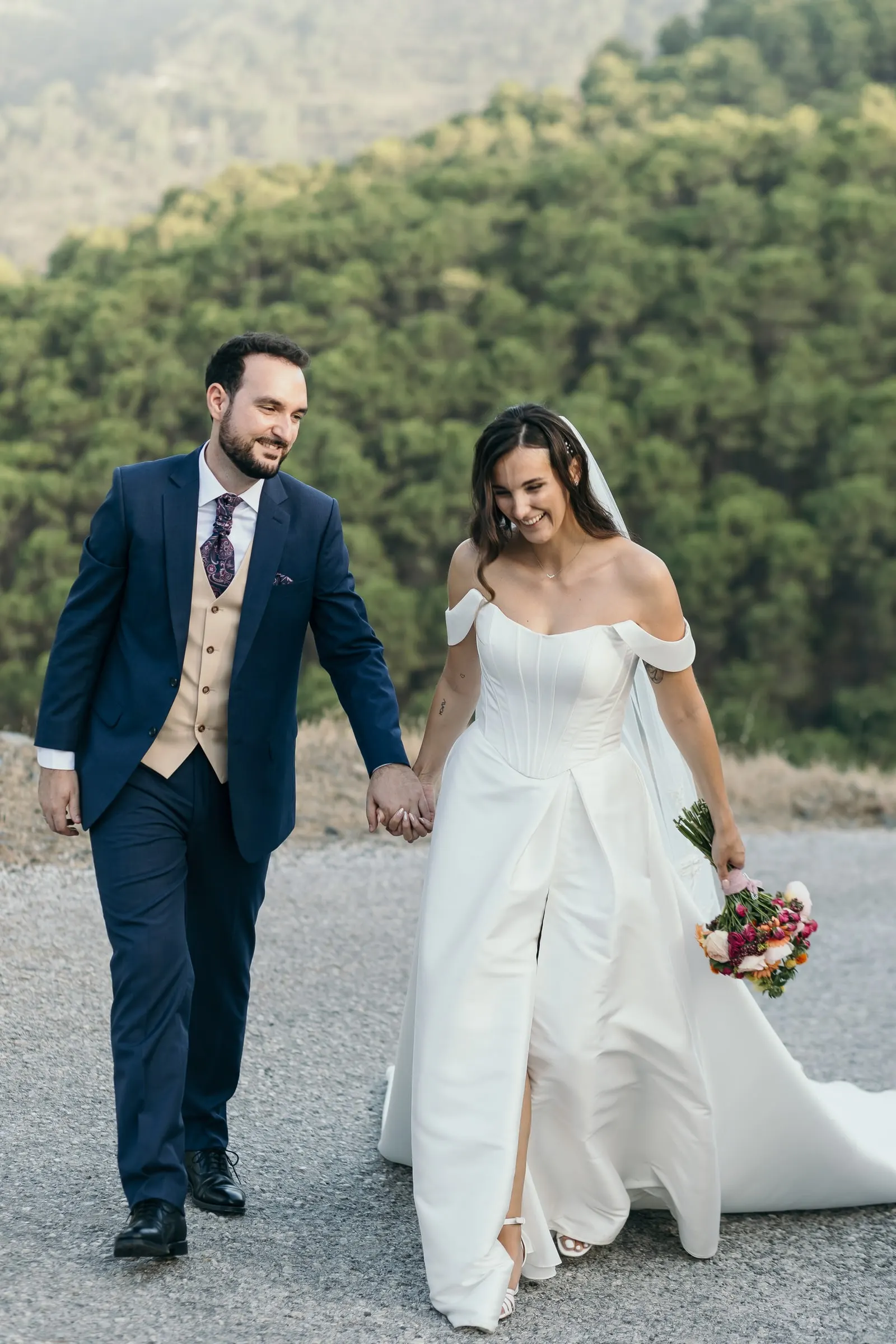 Bride and groom walking hand in hand on the road with forested hills behind