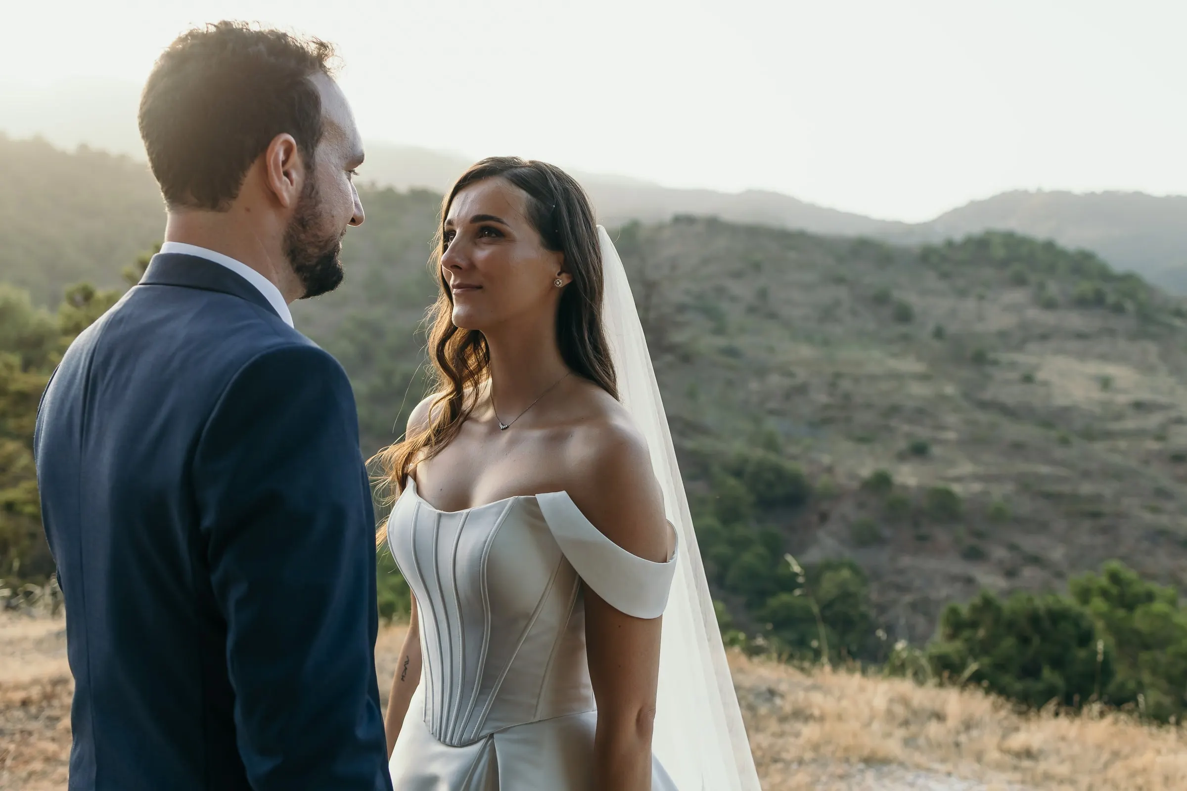 Groom and bride looking into each other's eyes against the evening hills