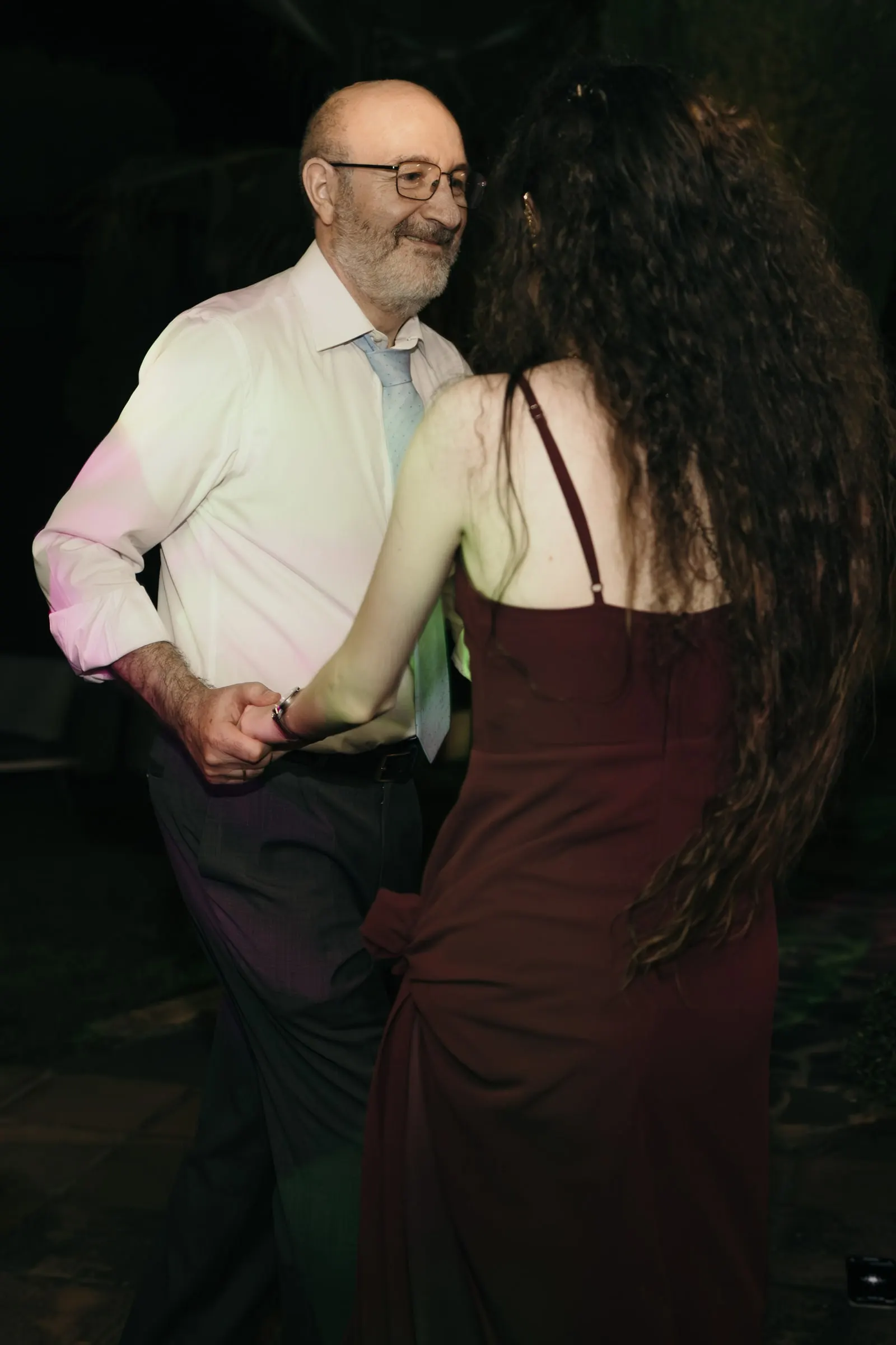 Older guest in glasses dancing with a woman in a long burgundy dress