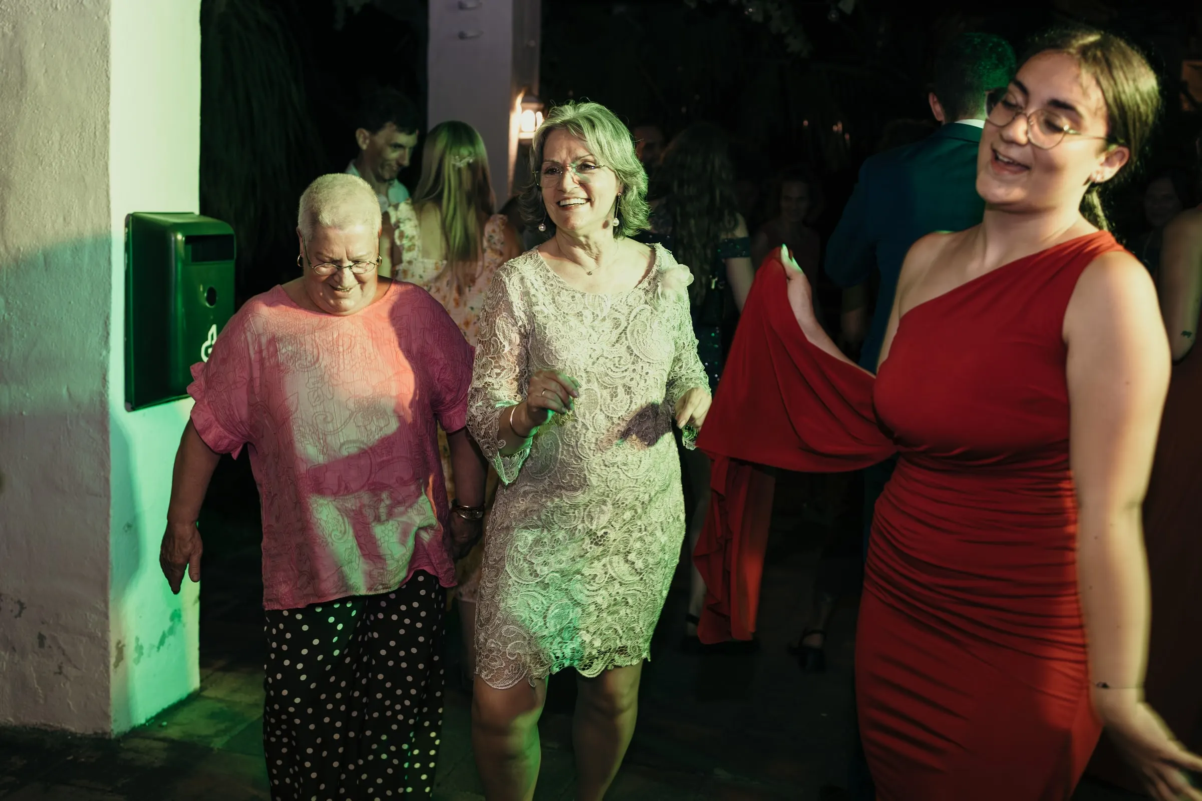 Older guests in pink and in lace dancing with a friend in a red dress