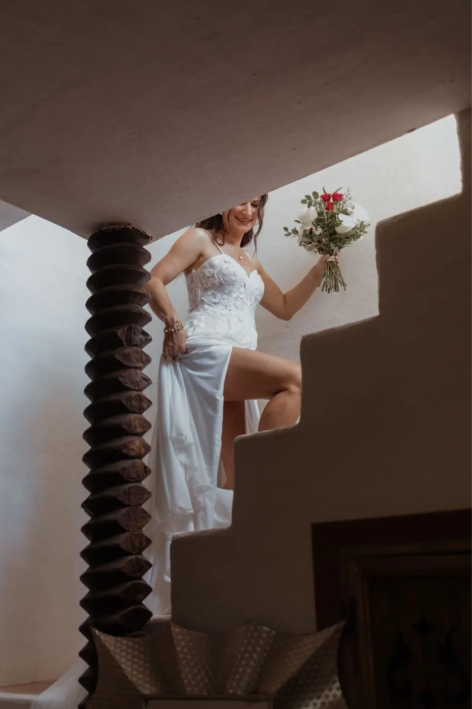 Bride lifting her skirt as she climbs a white staircase, bouquet in hand, seen from below, Costa del Sol
