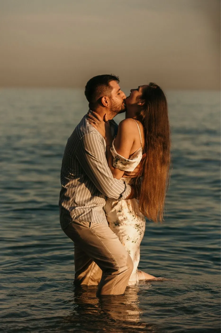 Couple kissing waist-deep in the sea in warm sunset light, the bride's long hair loose, Costa del Sol