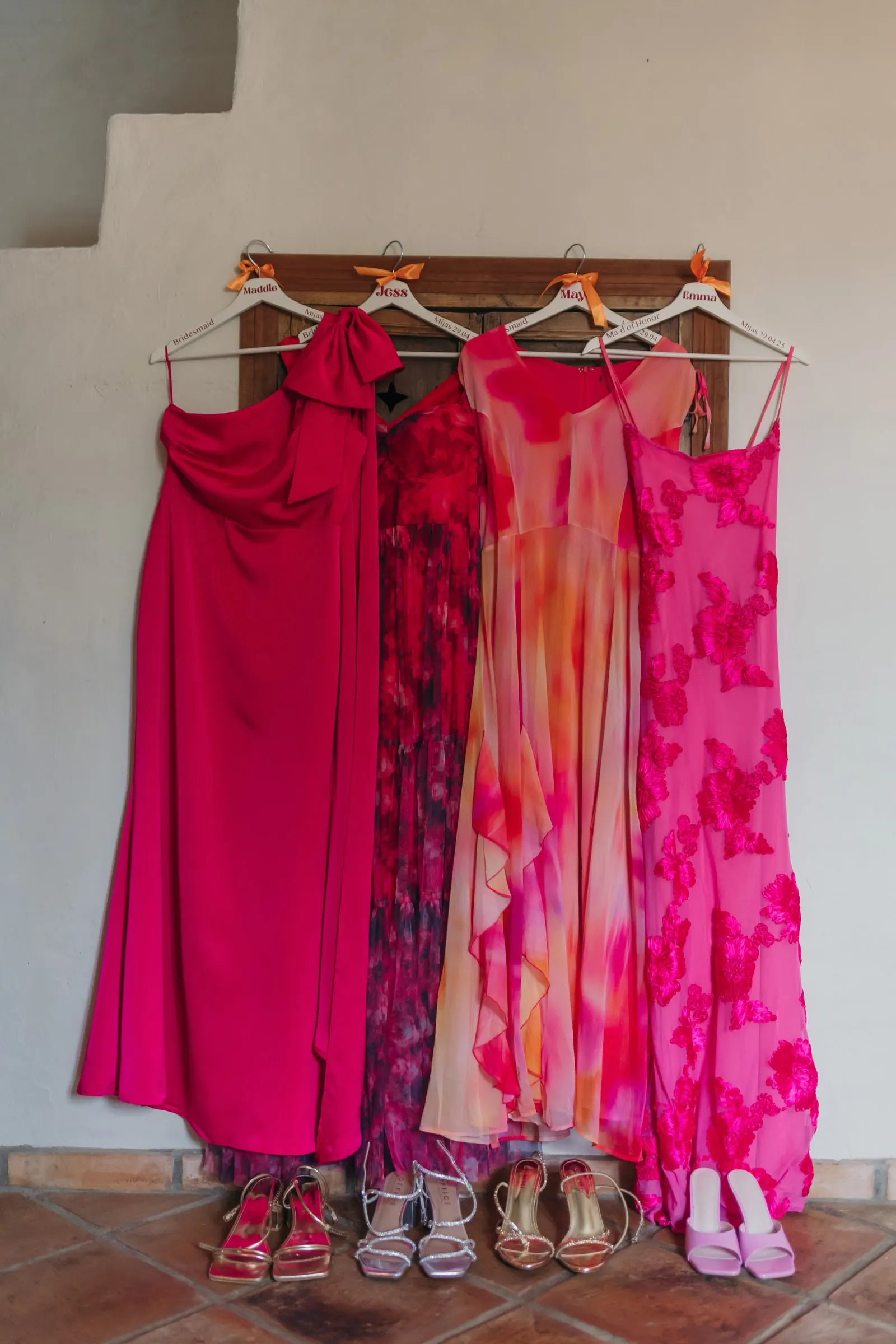 Bridesmaids' pink and coral dresses hanging on a wall above their shoes, Hacienda San José, Mijas