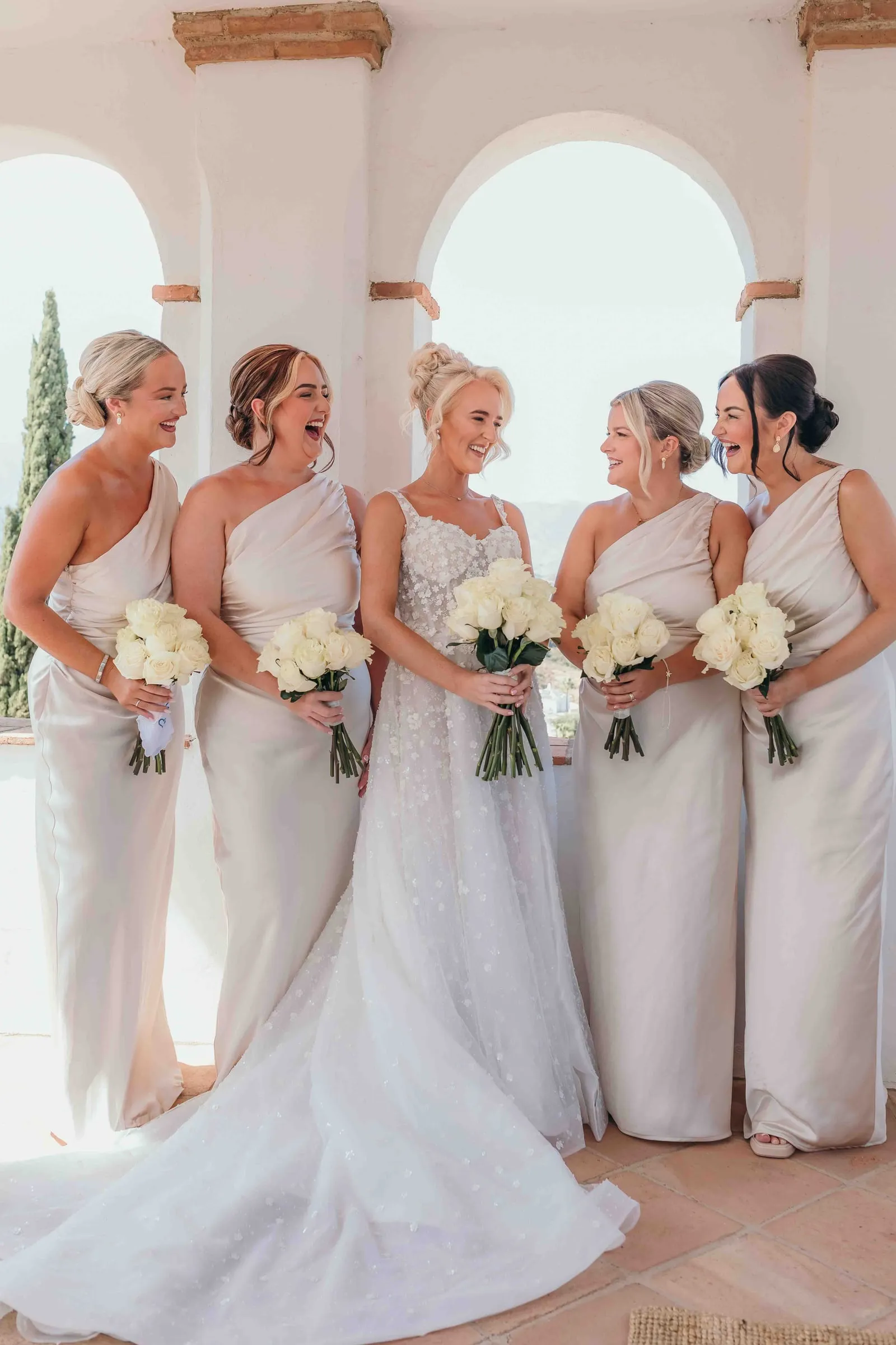 Bride and bridesmaids in white under the arches of a traditional hacienda in Mijas