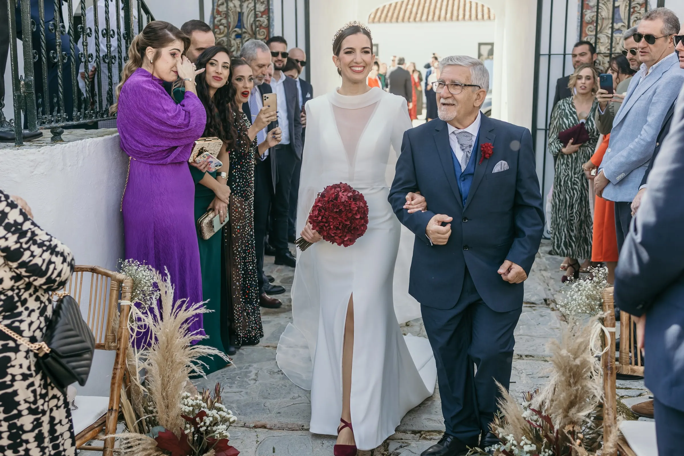 Bride walking down the aisle on her father's arm past guests and pampas grass in the cortijo courtyard