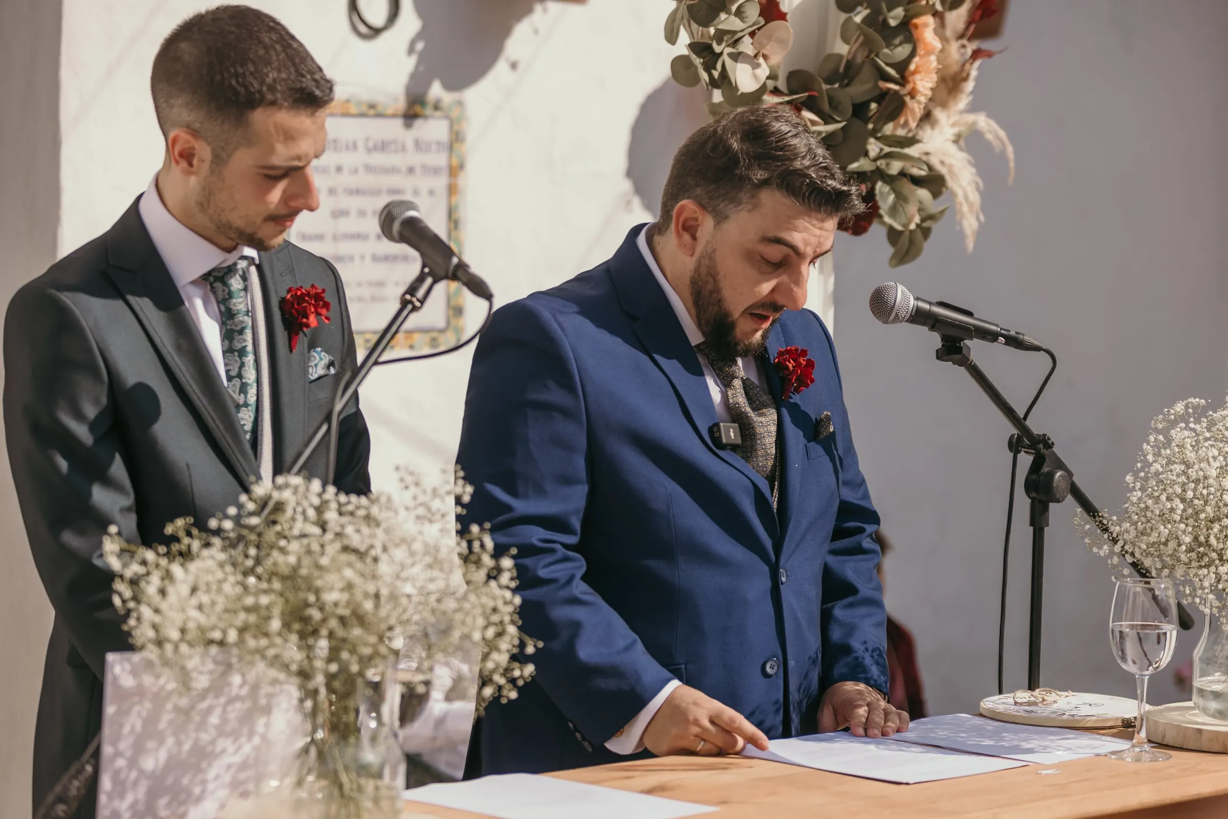 Friend of the couple reading his speech in front of a tiled plaque on the whitewashed wall