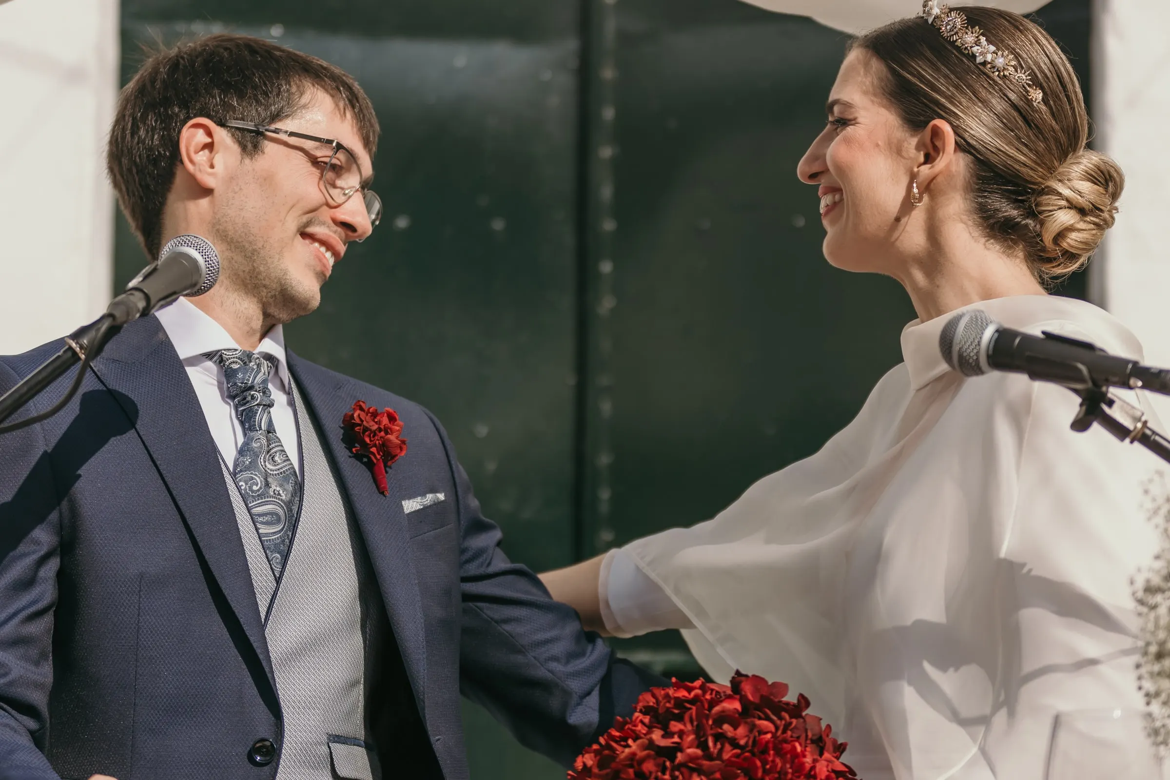 Groom laughing at the microphone as the bride reaches for his arm during their vows