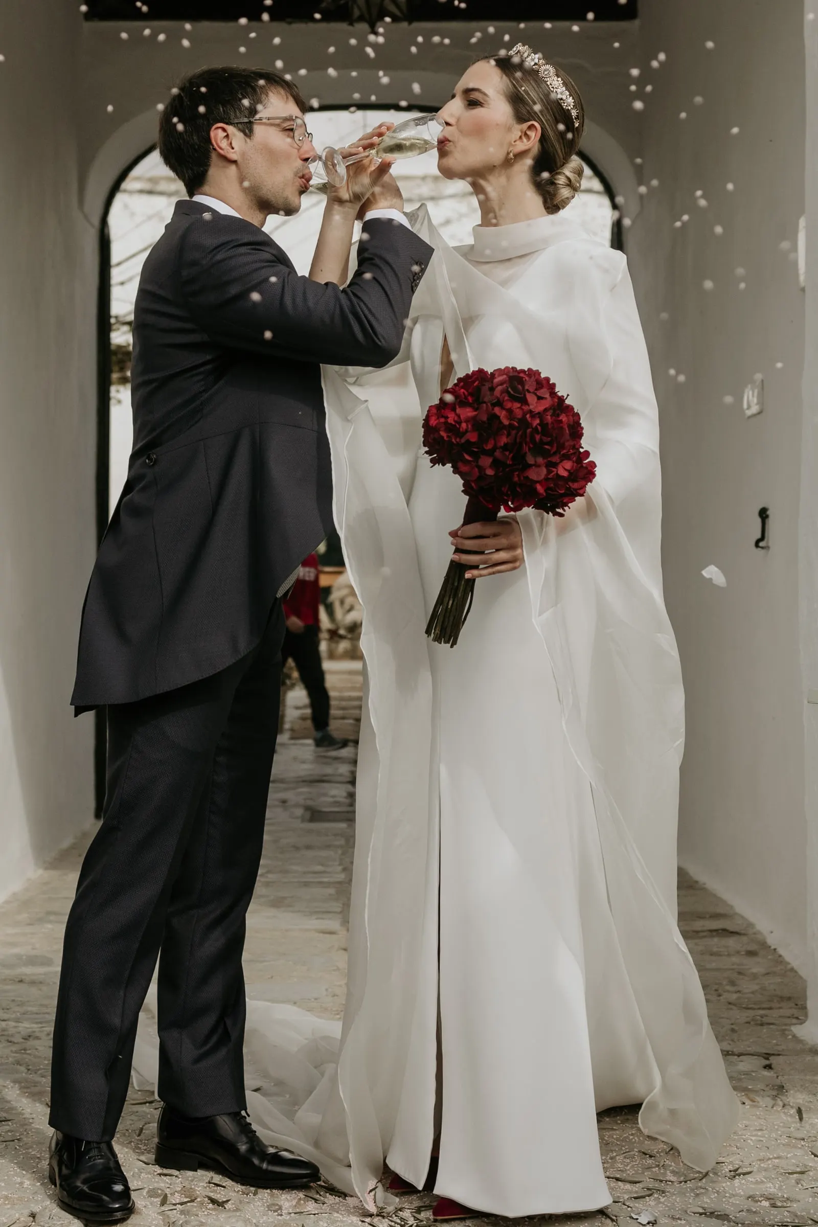 Bride and groom toasting under the arch with paper confetti falling around them