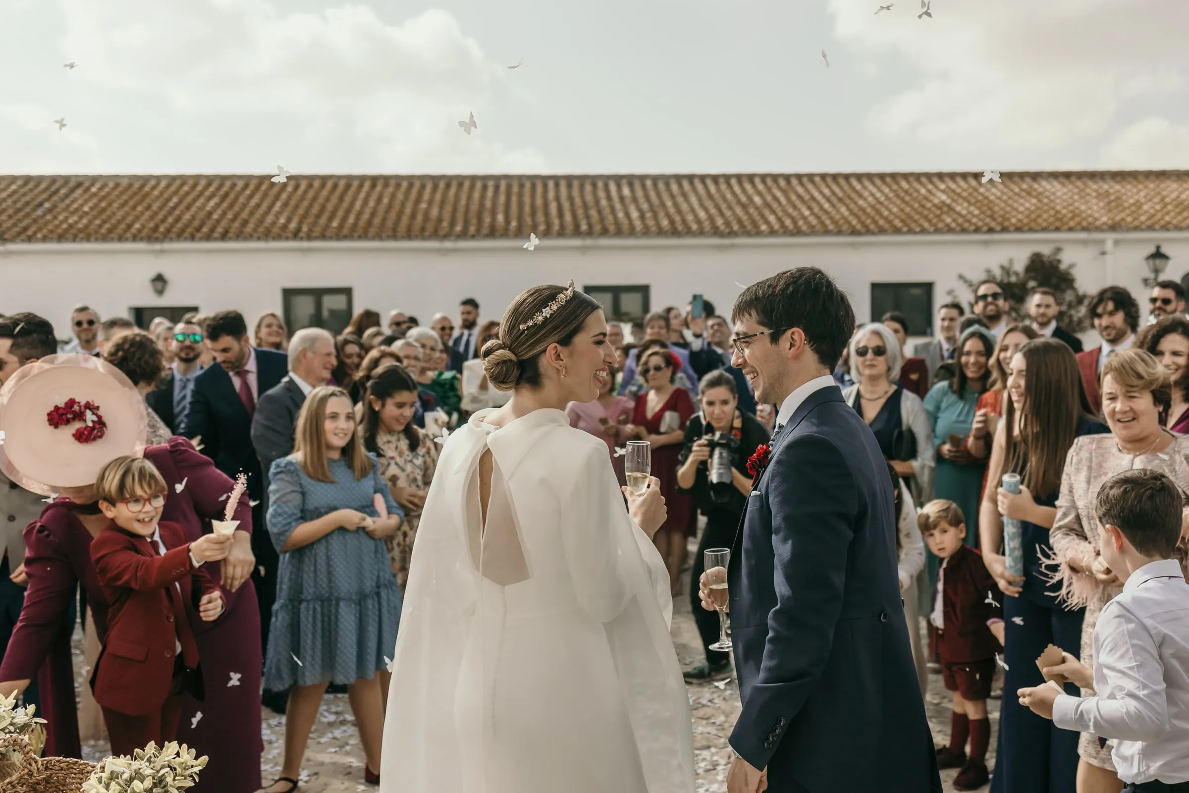 Couple walking into a crowd of guests in front of the long tiled roofs of the Andalusian cortijo