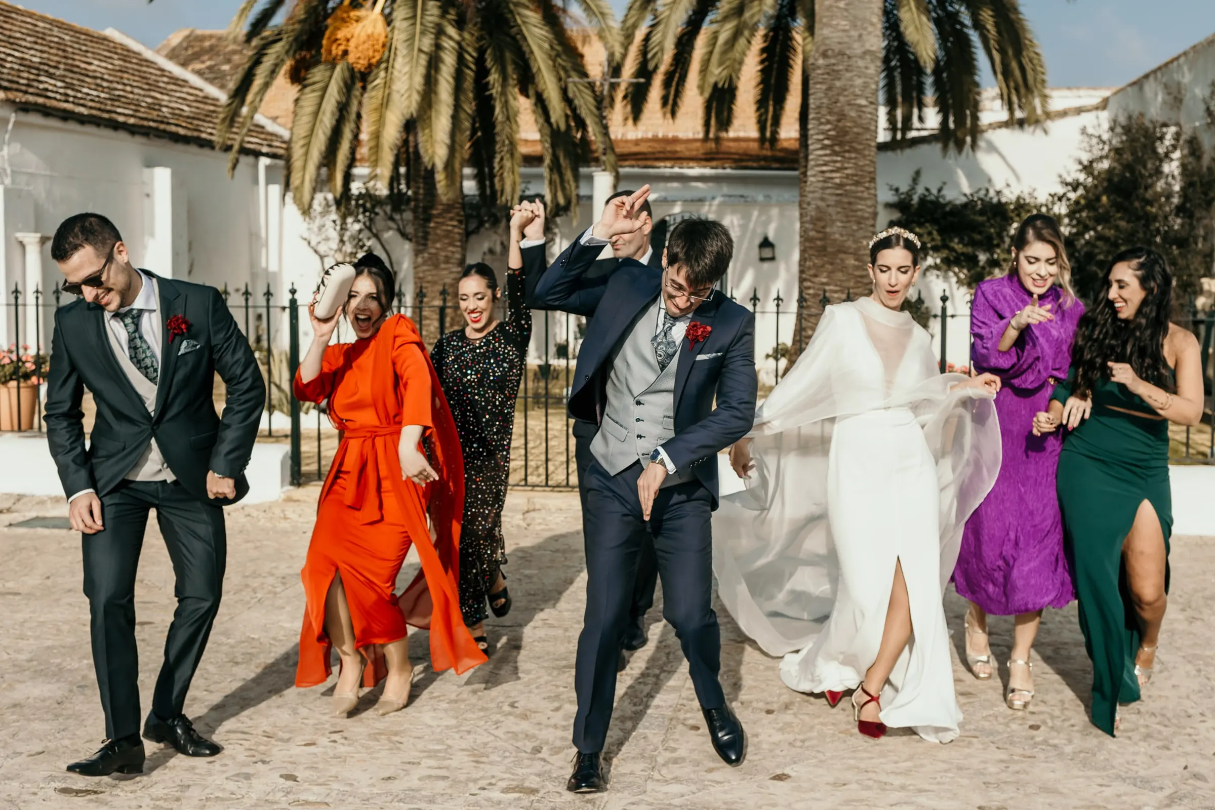 Bride, groom and friends dancing under the palm trees in front of the white cortijo