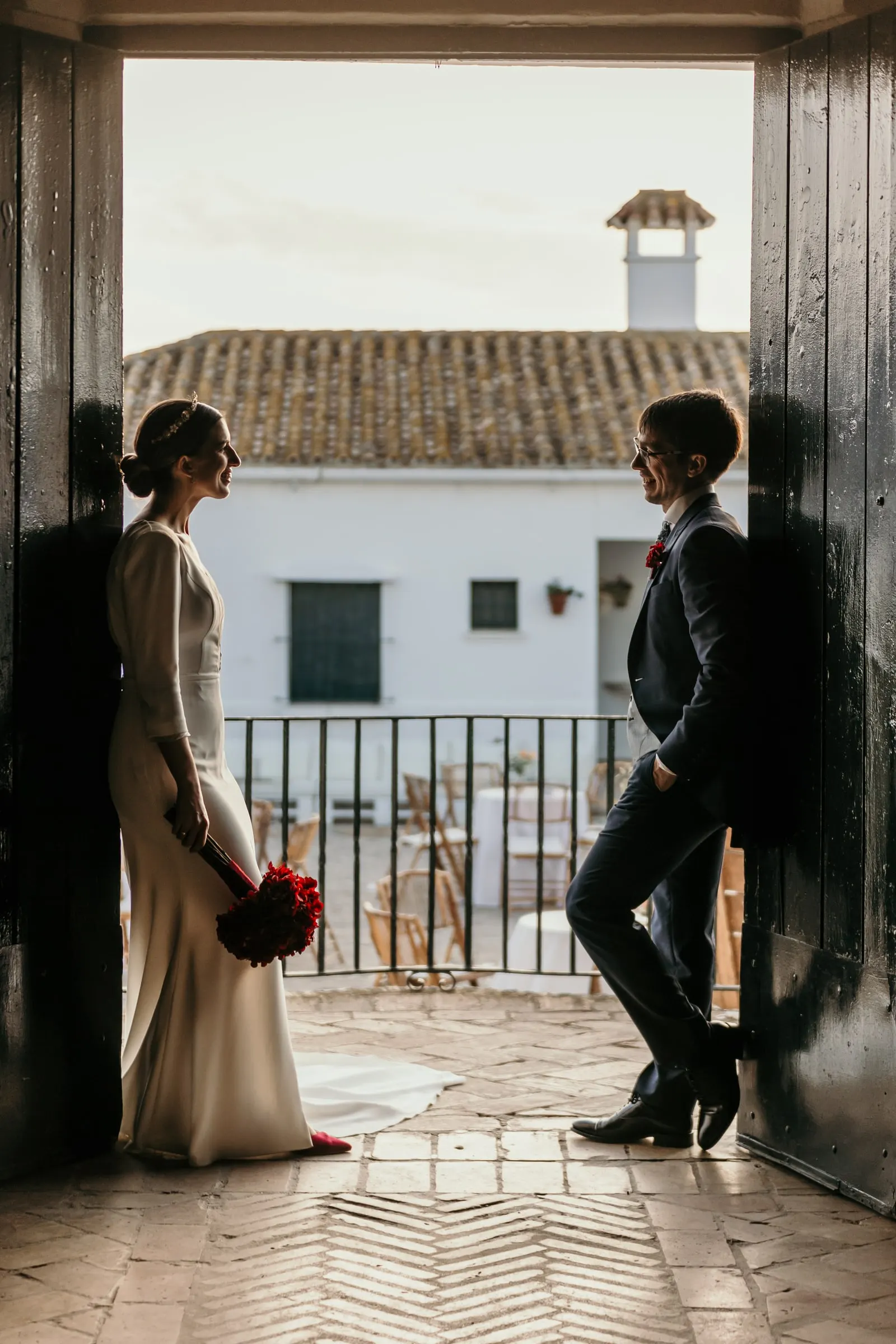 Bride and groom framed by a dark doorway with the white cortijo and its tiled roof behind