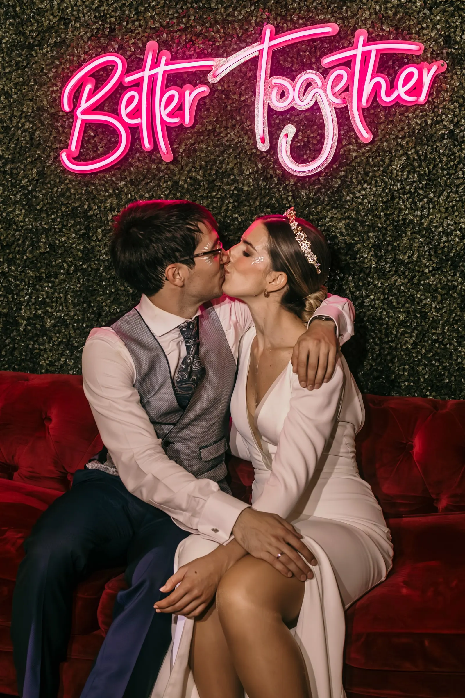 Couple kissing on a red velvet sofa under a pink 'Better Together' neon sign