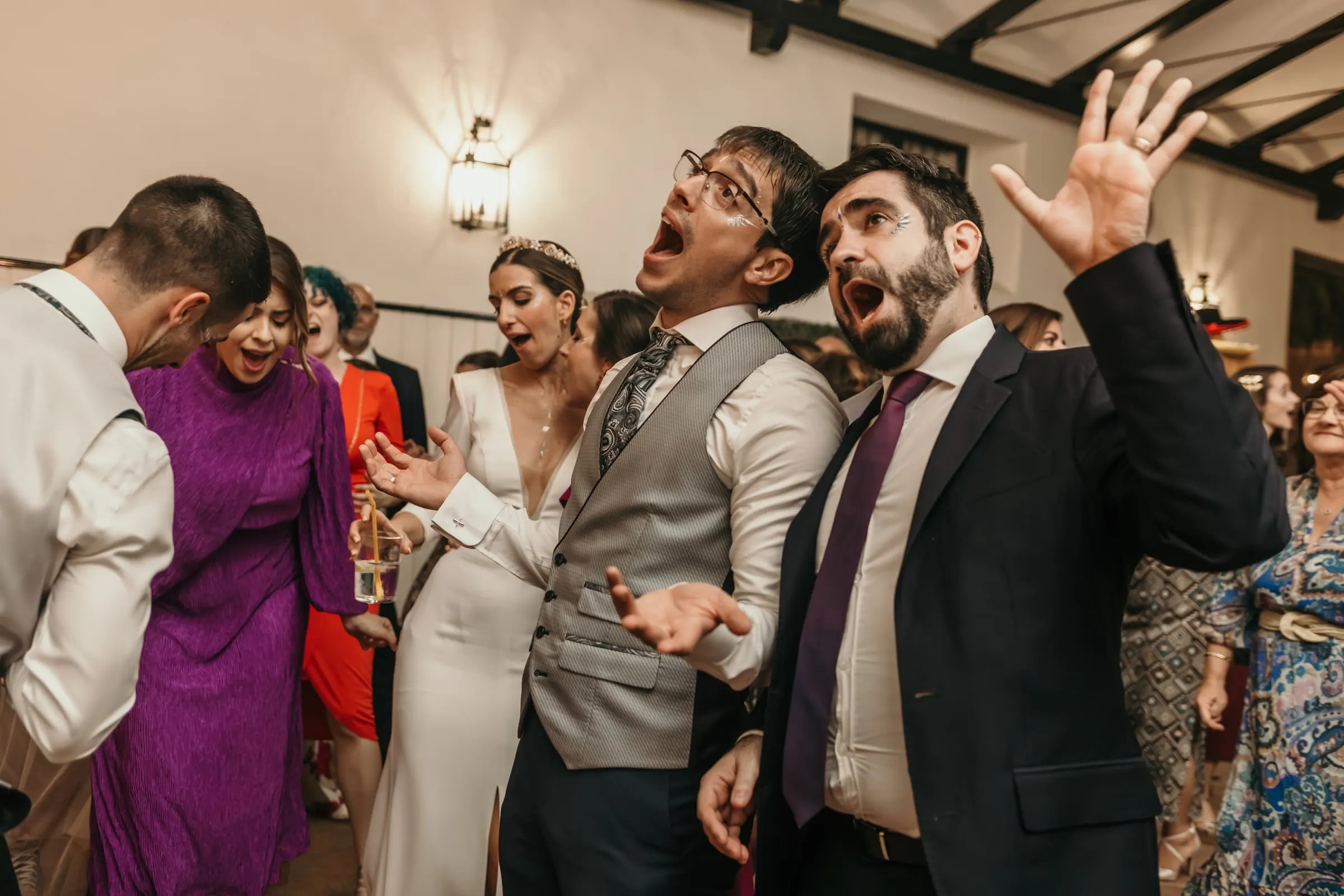 Groom and friends singing with their arms in the air while the bride laughs beside them