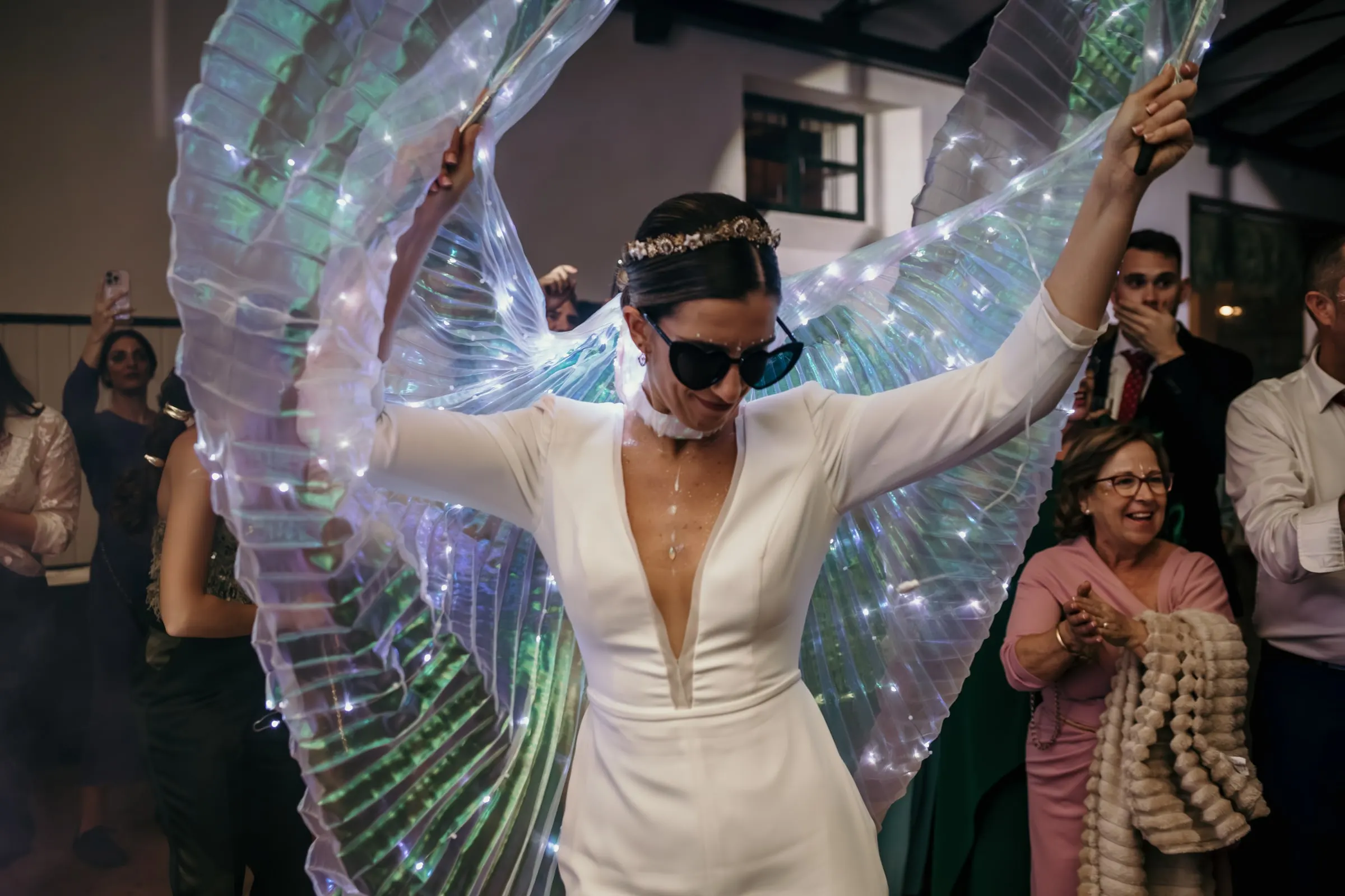 Bride in sunglasses opening a pair of glowing LED wings on the dance floor