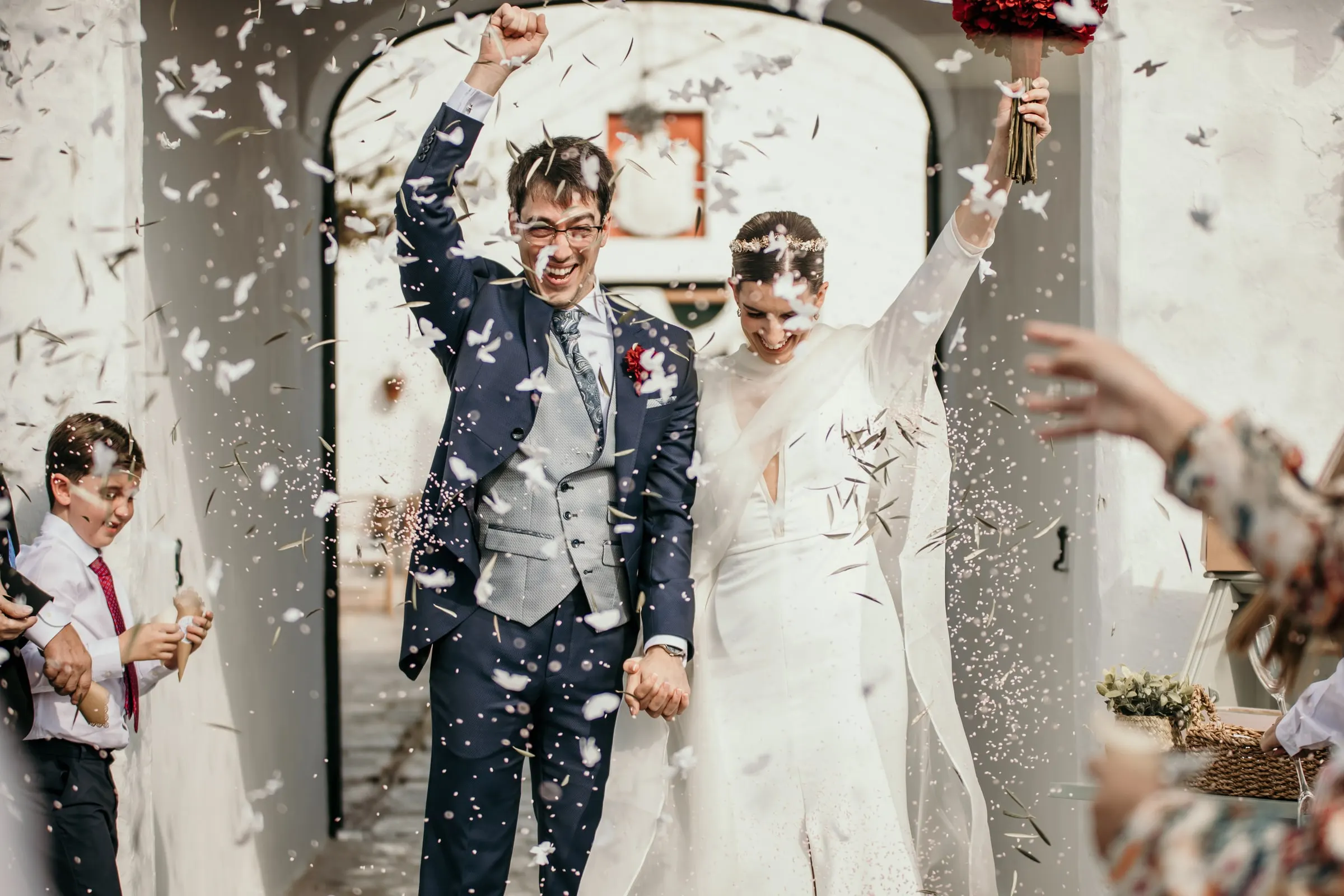 Groom punching the air and bride raising her arm as paper confetti rains down at the cortijo archway