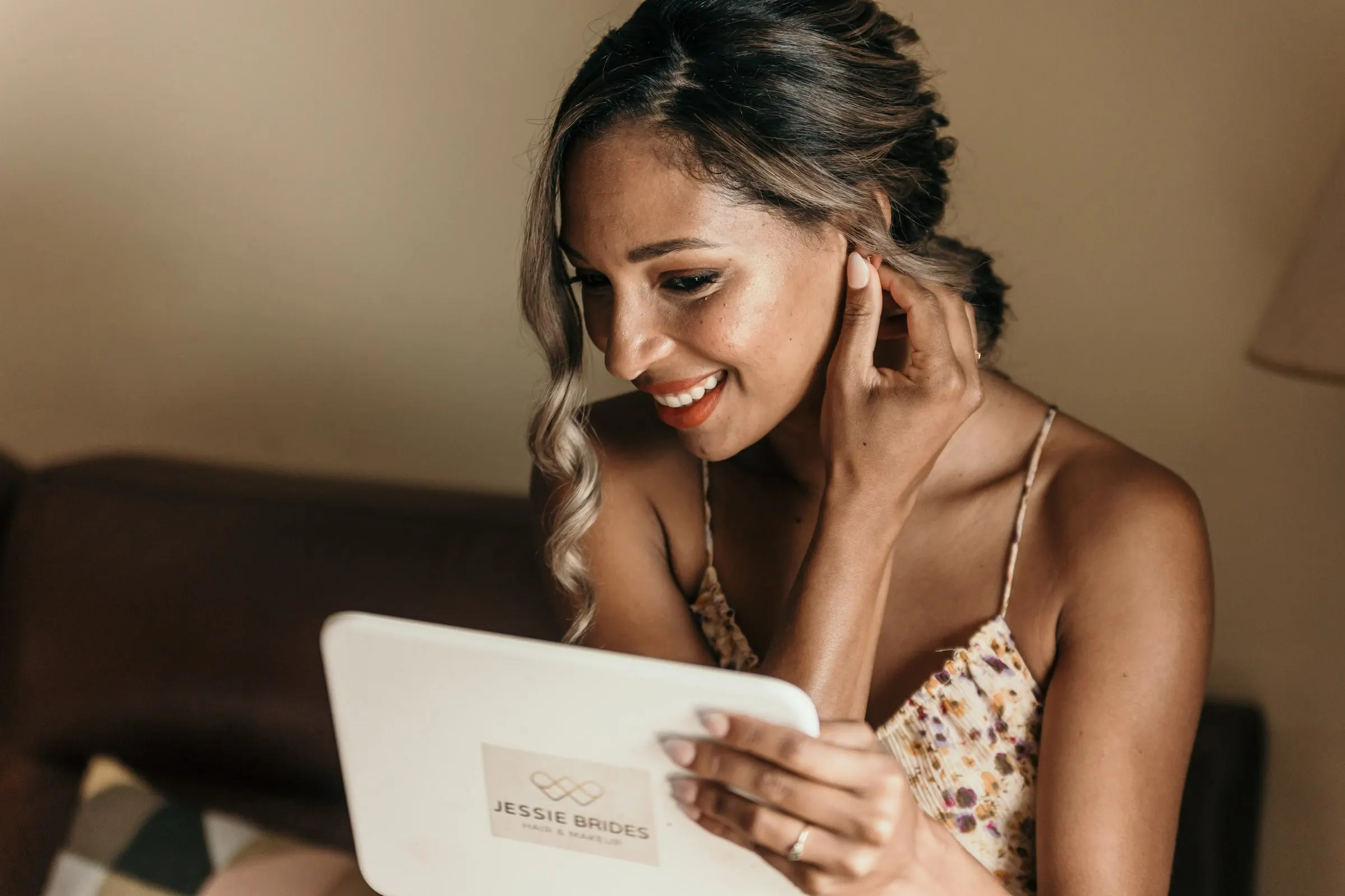 Bride touching her earring and smiling at the mirror after hair and make-up on the wedding morning
