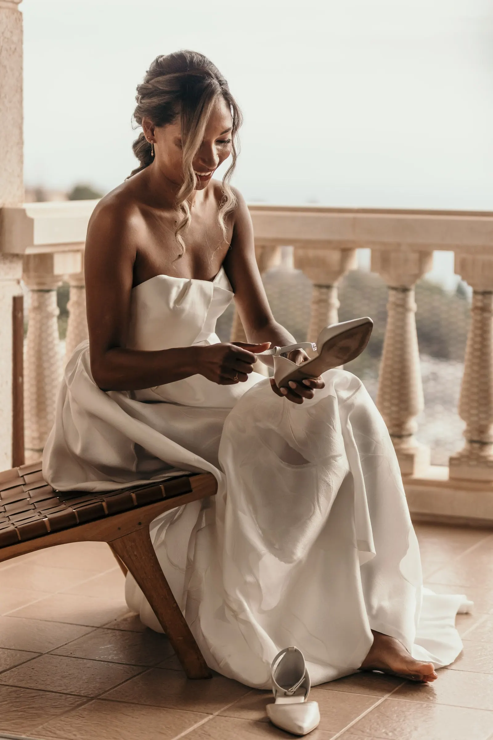 Bride sitting on a wooden bench on the balcony putting on her shoes