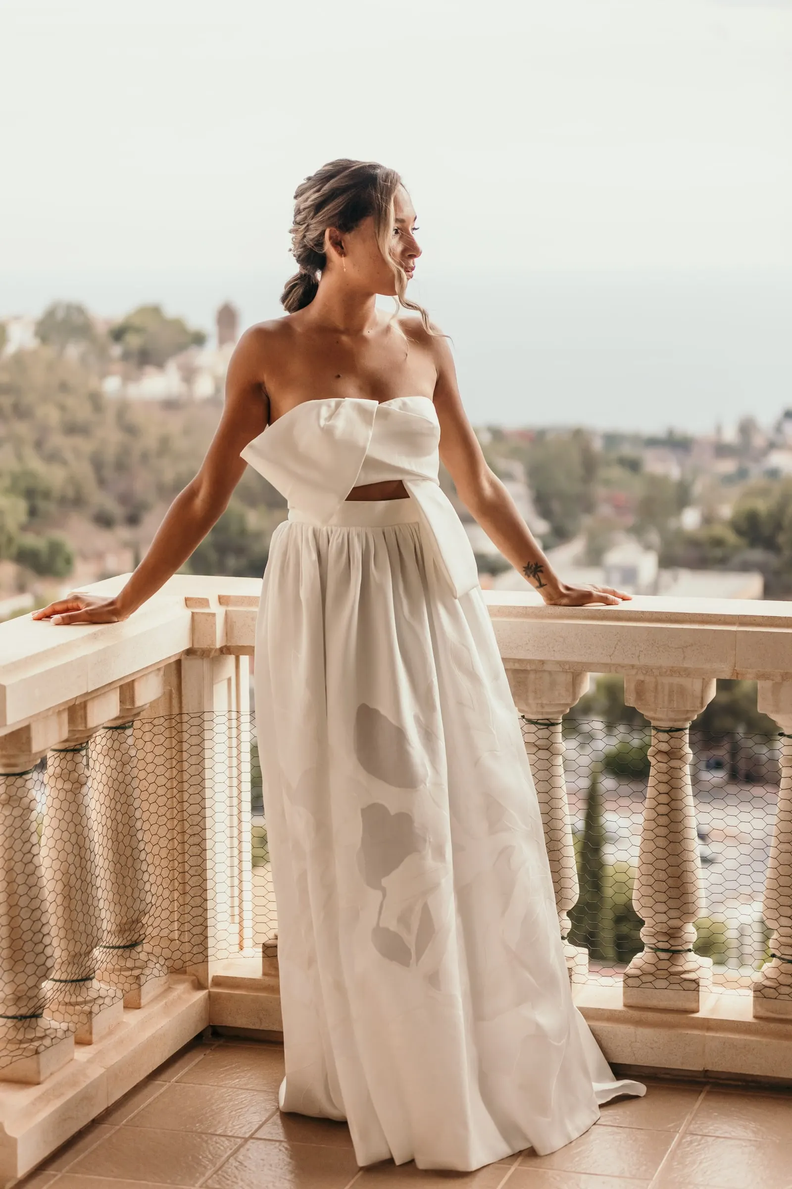 Bride in a strapless bow-front gown leaning on the white balustrade of the villa