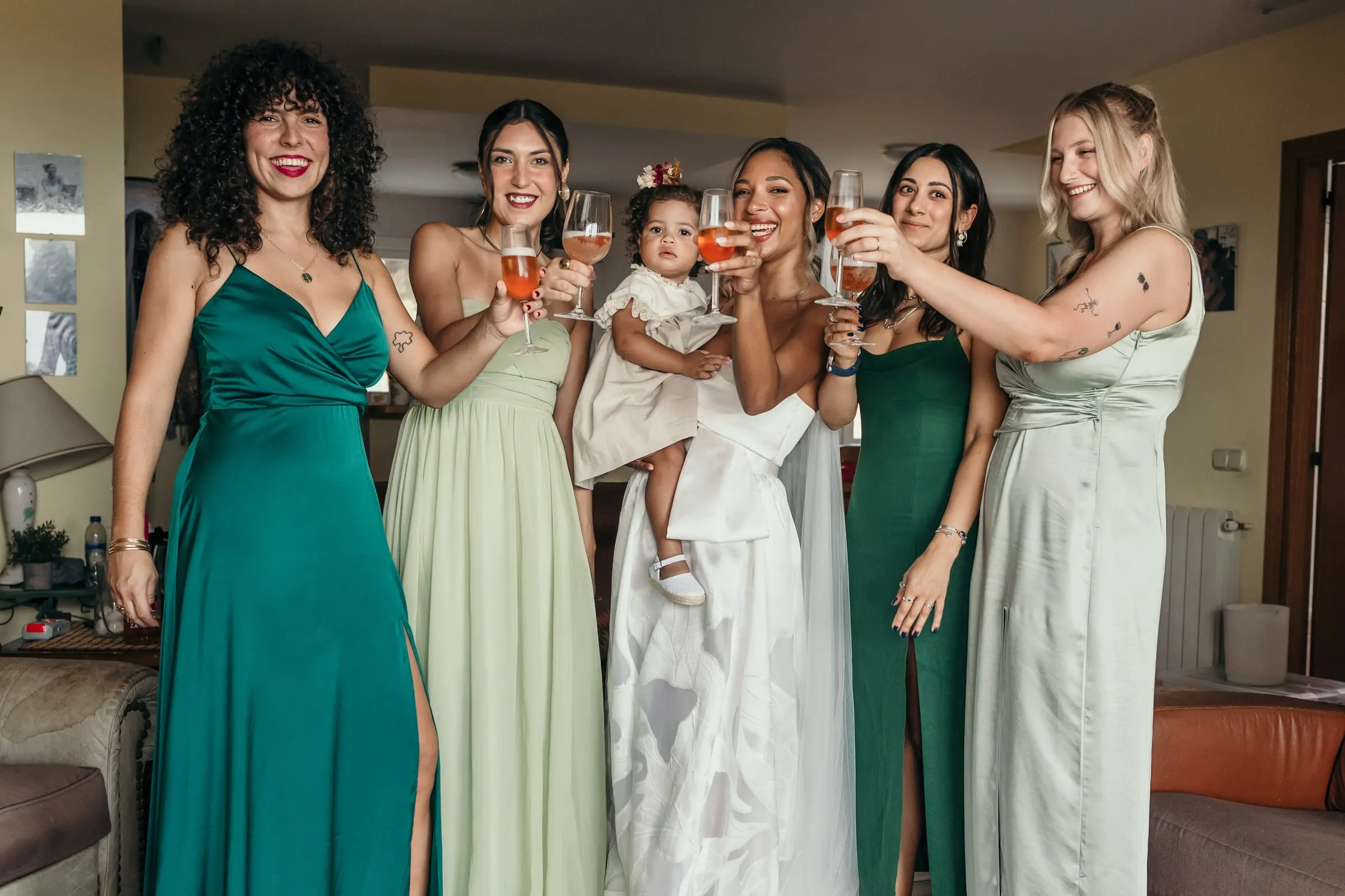 Bridesmaids in green and sage dresses toasting with the bride and the little girl in the living room