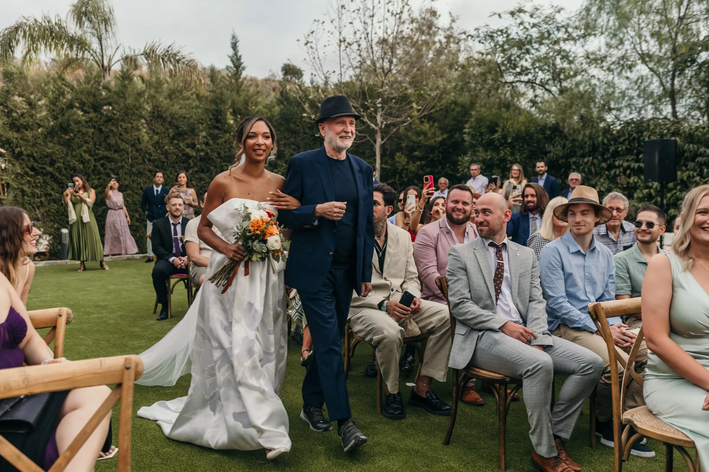 Wide view of the bride walking down the aisle between the guests in the garden
