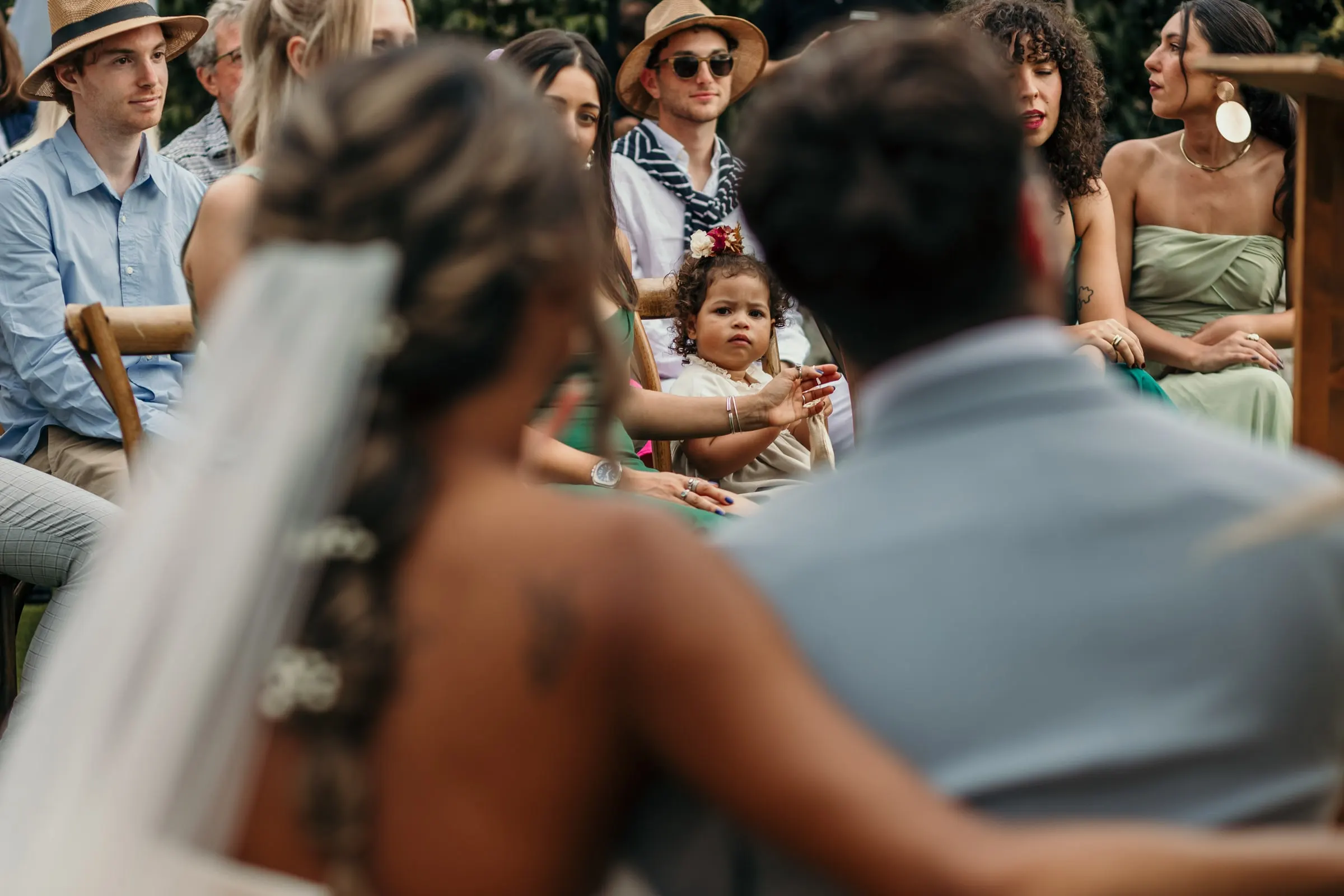 Bride's veil and braid in the foreground as she looks back at the guests