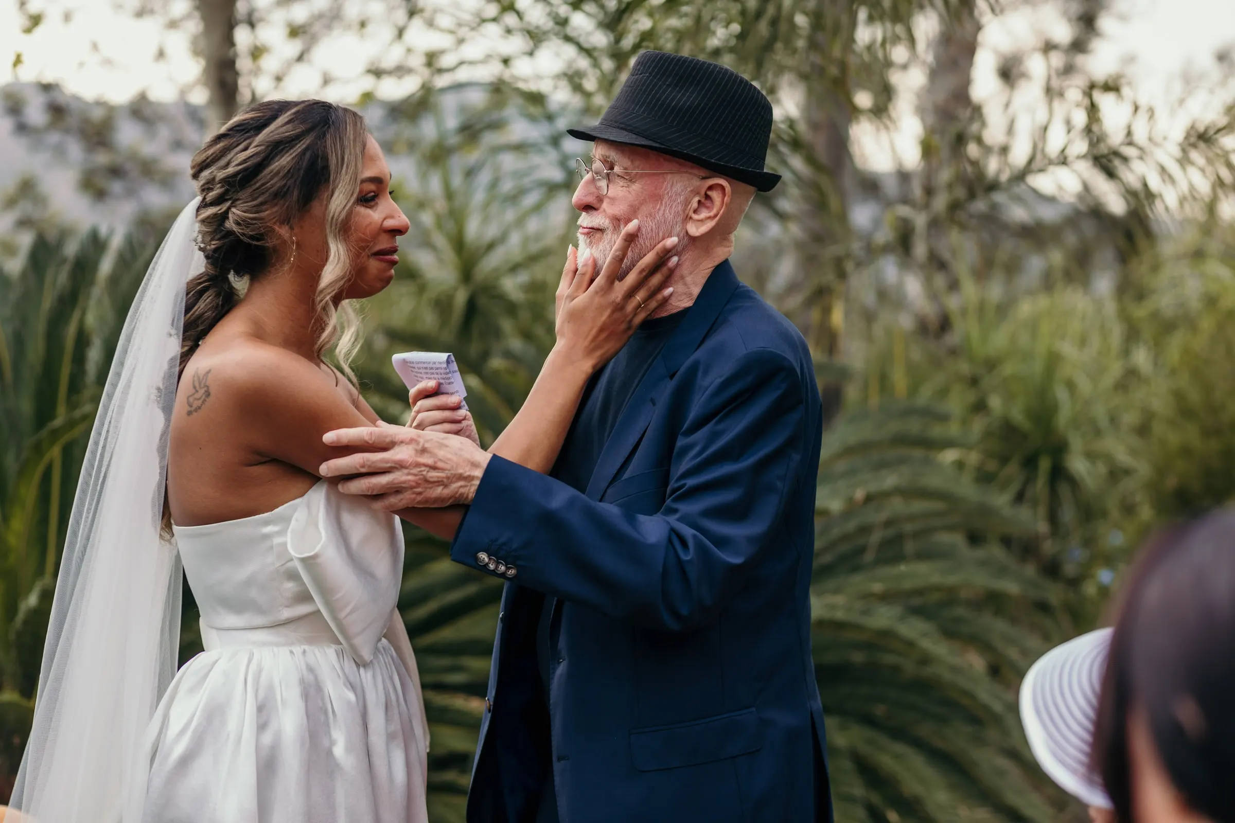 Bride cupping the face of the man in the black hat during the ceremony