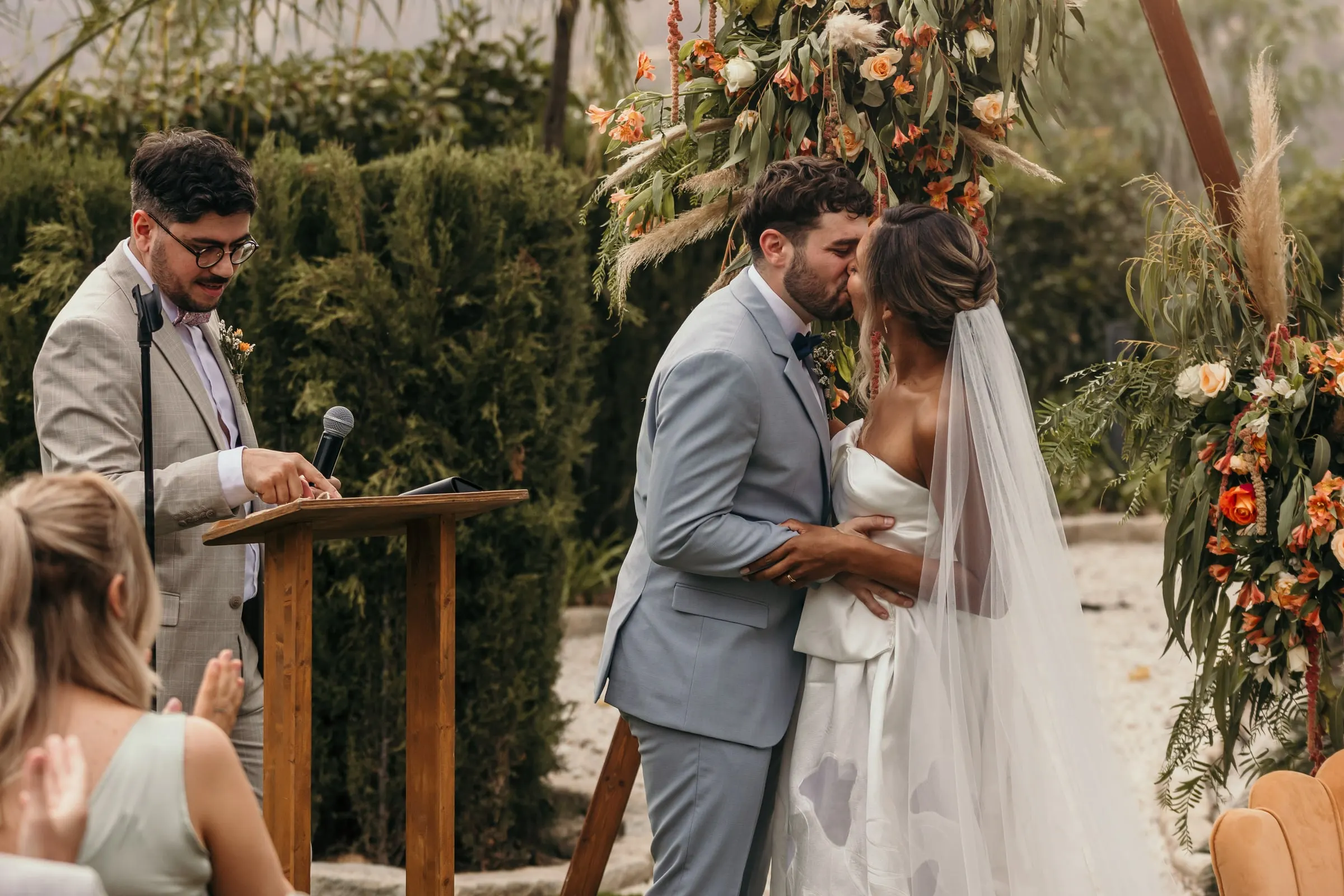 First kiss at the outdoor ceremony beside the wooden lectern and orange flowers