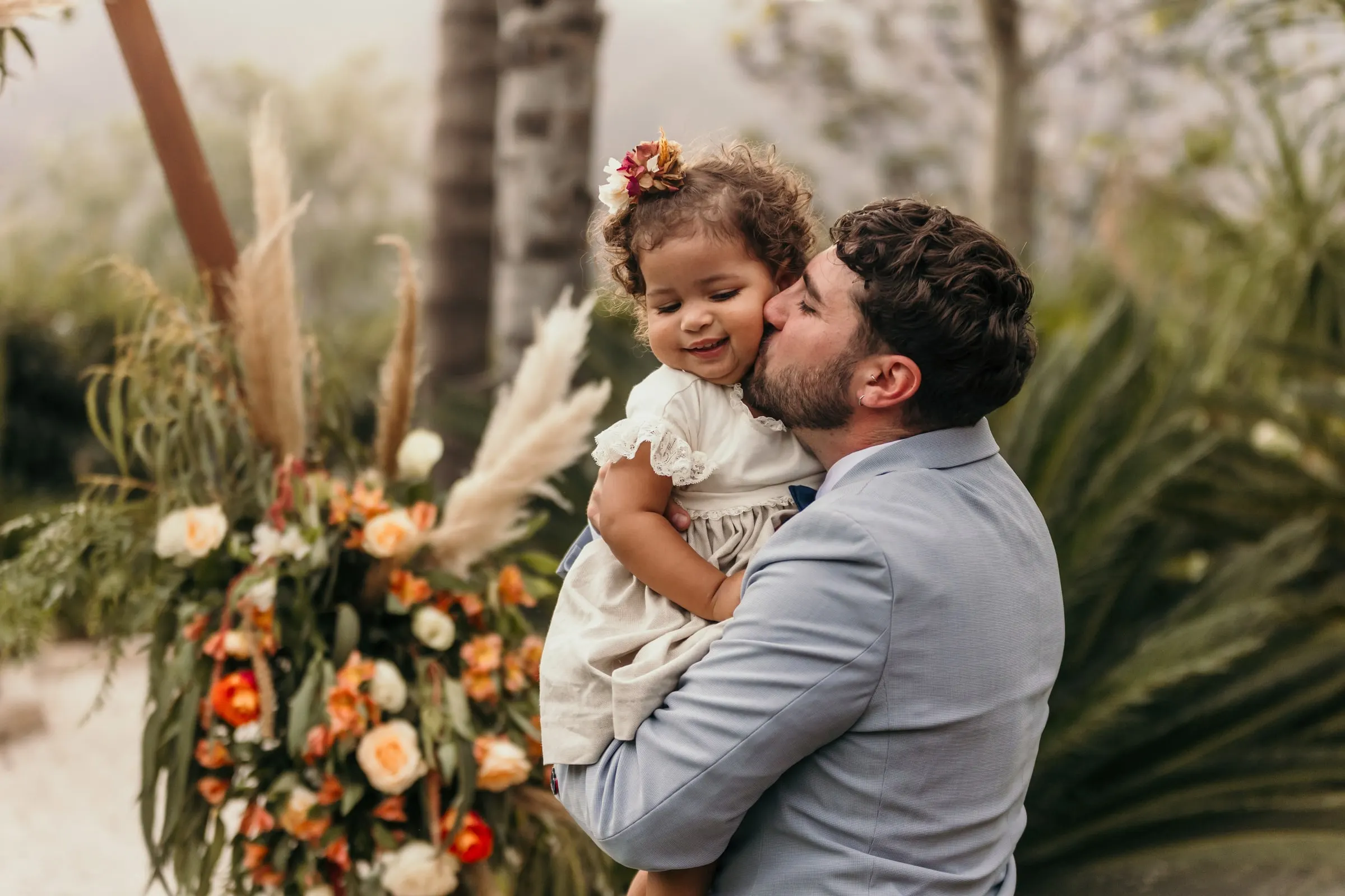 Groom kissing the little girl's cheek beside the pampas and rose arrangement