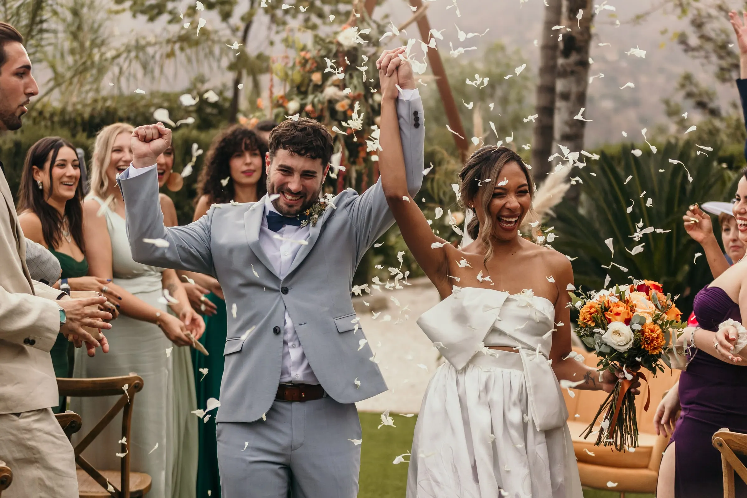 Newlyweds cheering as guests throw petals at the end of the ceremony