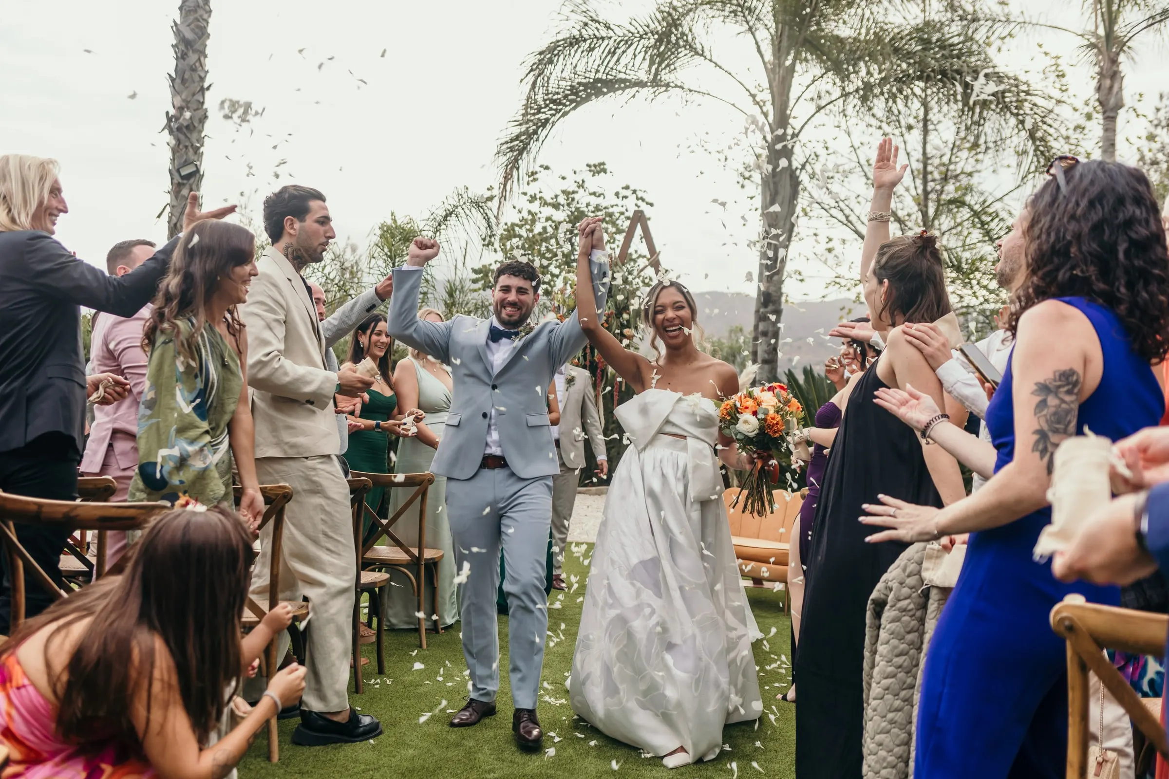 Bride and groom walking back up the aisle under a shower of petals among the palm trees