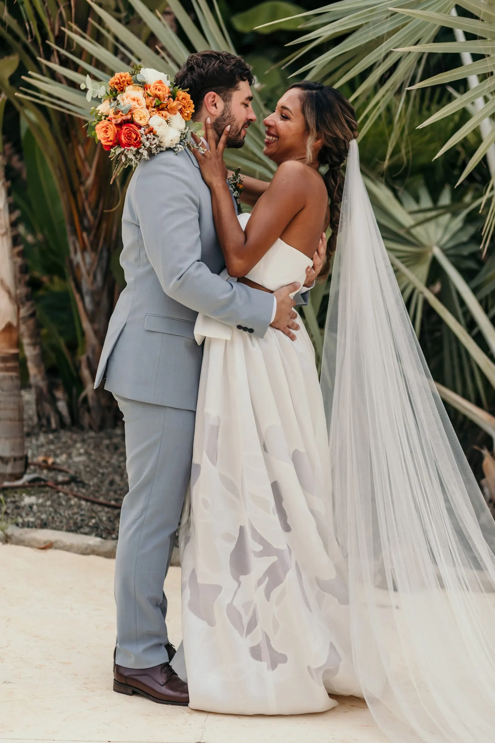 Groom embracing the bride in her long veil in the palm garden